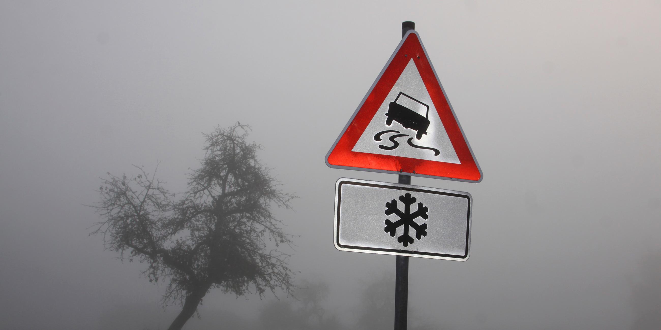 Ein Verkehrsschild im Nebel warnt vor Schleudergefahr