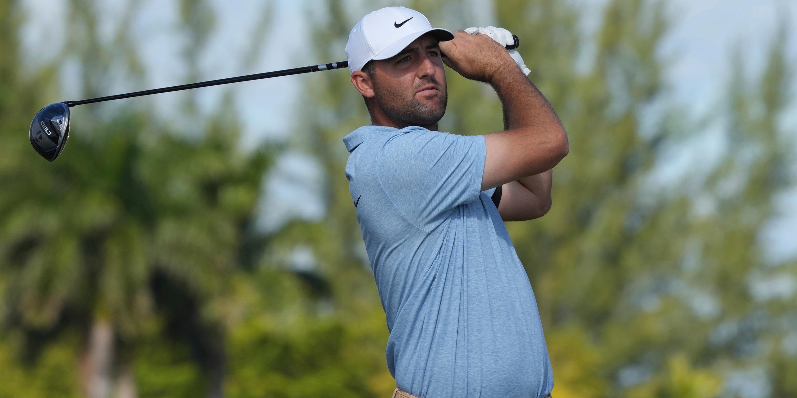 Der Golfer Scottie Scheffler nach seinem Schlag. Er schaut dem Ball nach und hält seinen Schläger hinter seinem Kopf.