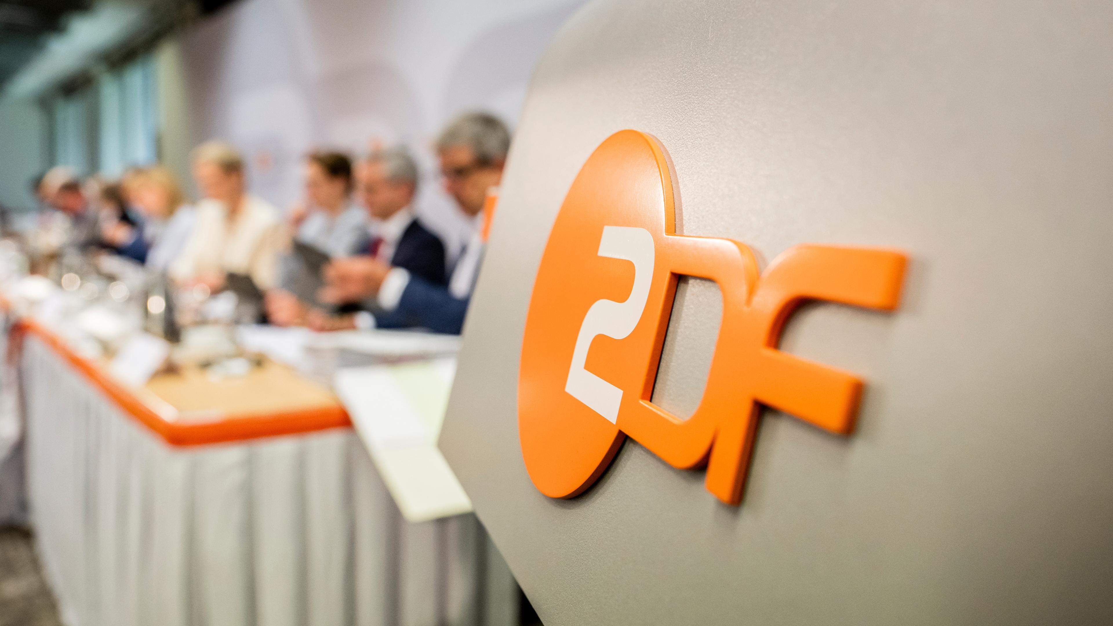 Nahaufnahme Rednerpult mit ZDF-Logo während einer ZDF-Fernsehratssitzung, im Hintergrund unscharf Geschäftsleitungsmitglieder des ZDF.