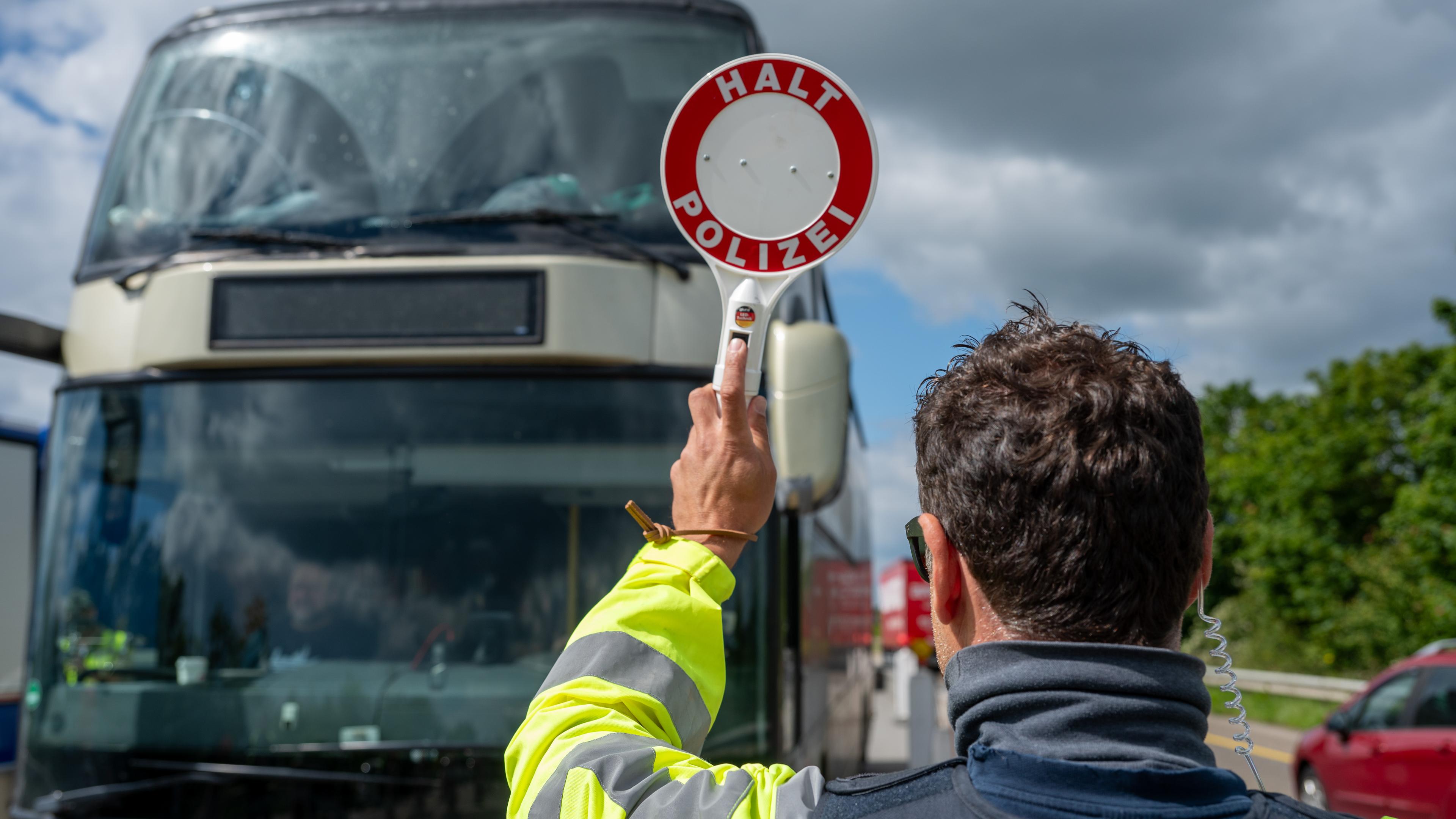 Ein Bundespolizist hält auf der A64 mit einer Kelle einen Reisebus an.