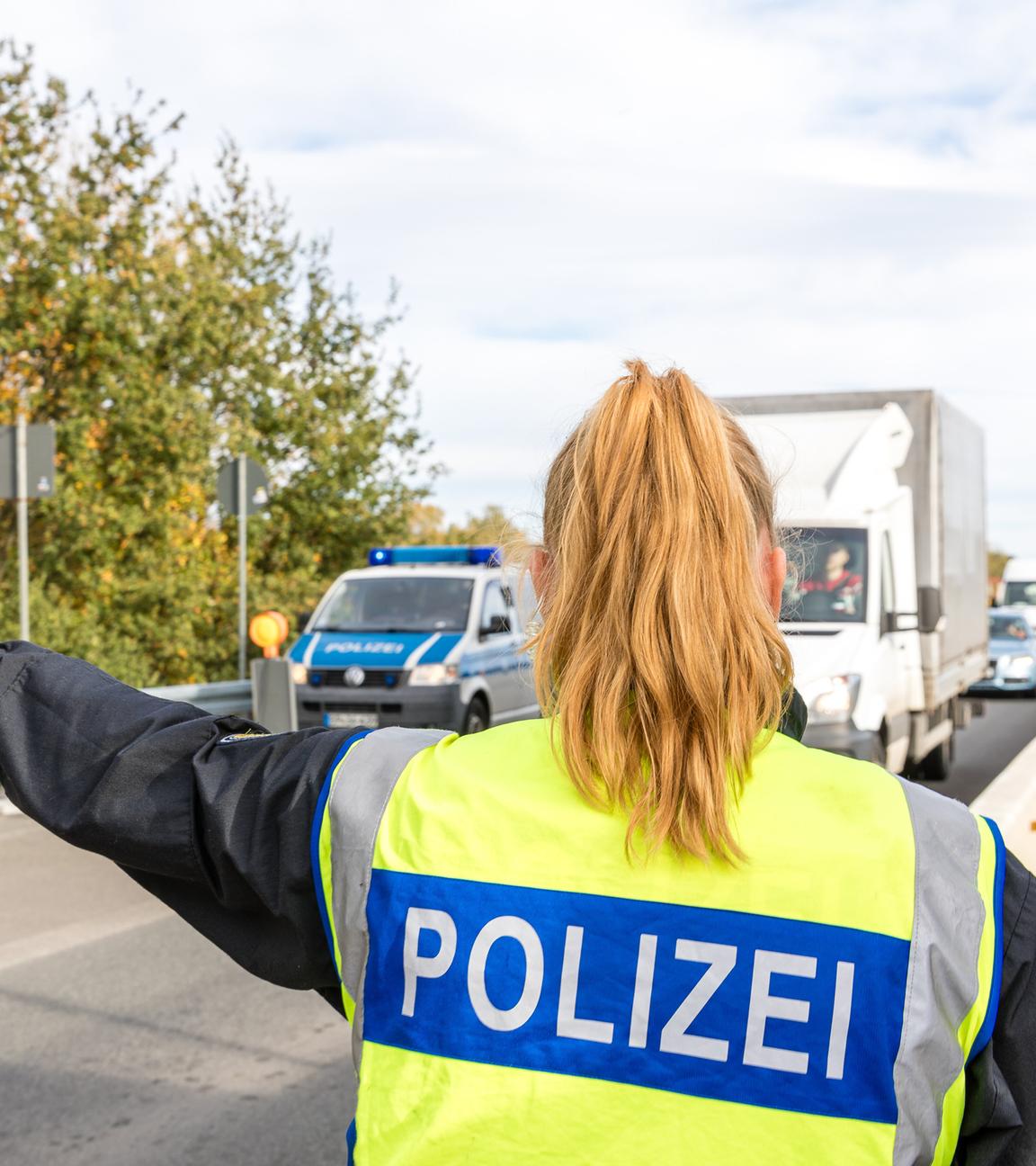 Eine Polizisten von hinten stoppt mit einer Kelle Fahrzeuge auf der Autobahn 15 vor dem Grenzübergang nach Frankreich.