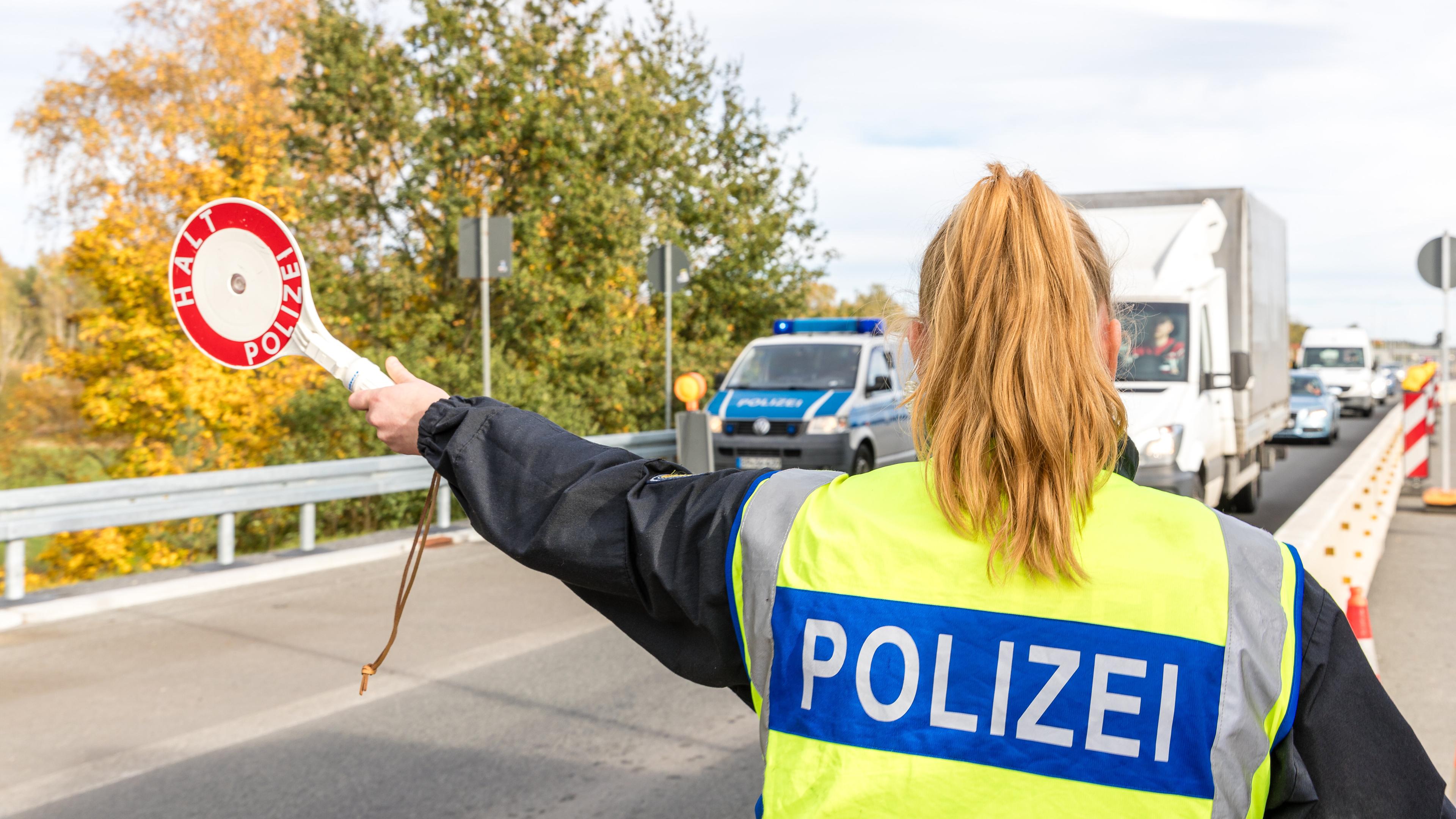 Eine Polizisten von hinten stoppt mit einer Kelle Fahrzeuge auf der Autobahn 15 vor dem Grenzübergang nach Frankreich.