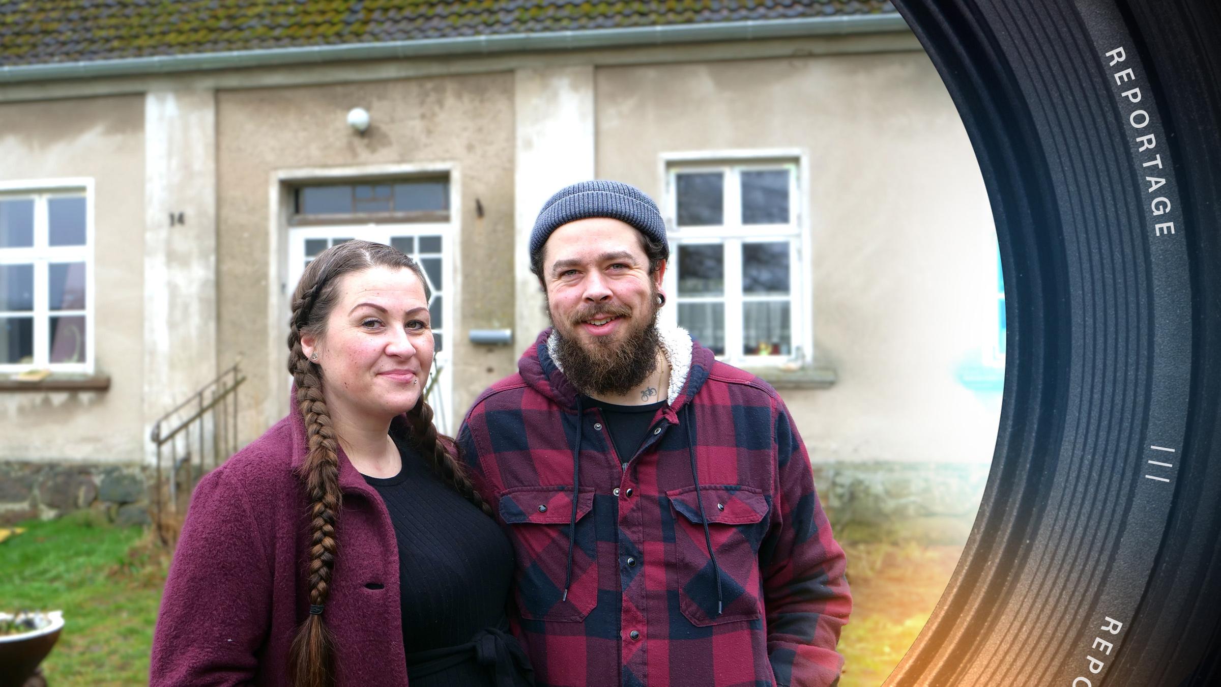 Sara und Max stehen nebeneinander vor einem alten Haus und blicken lächelnd in die Kamera.