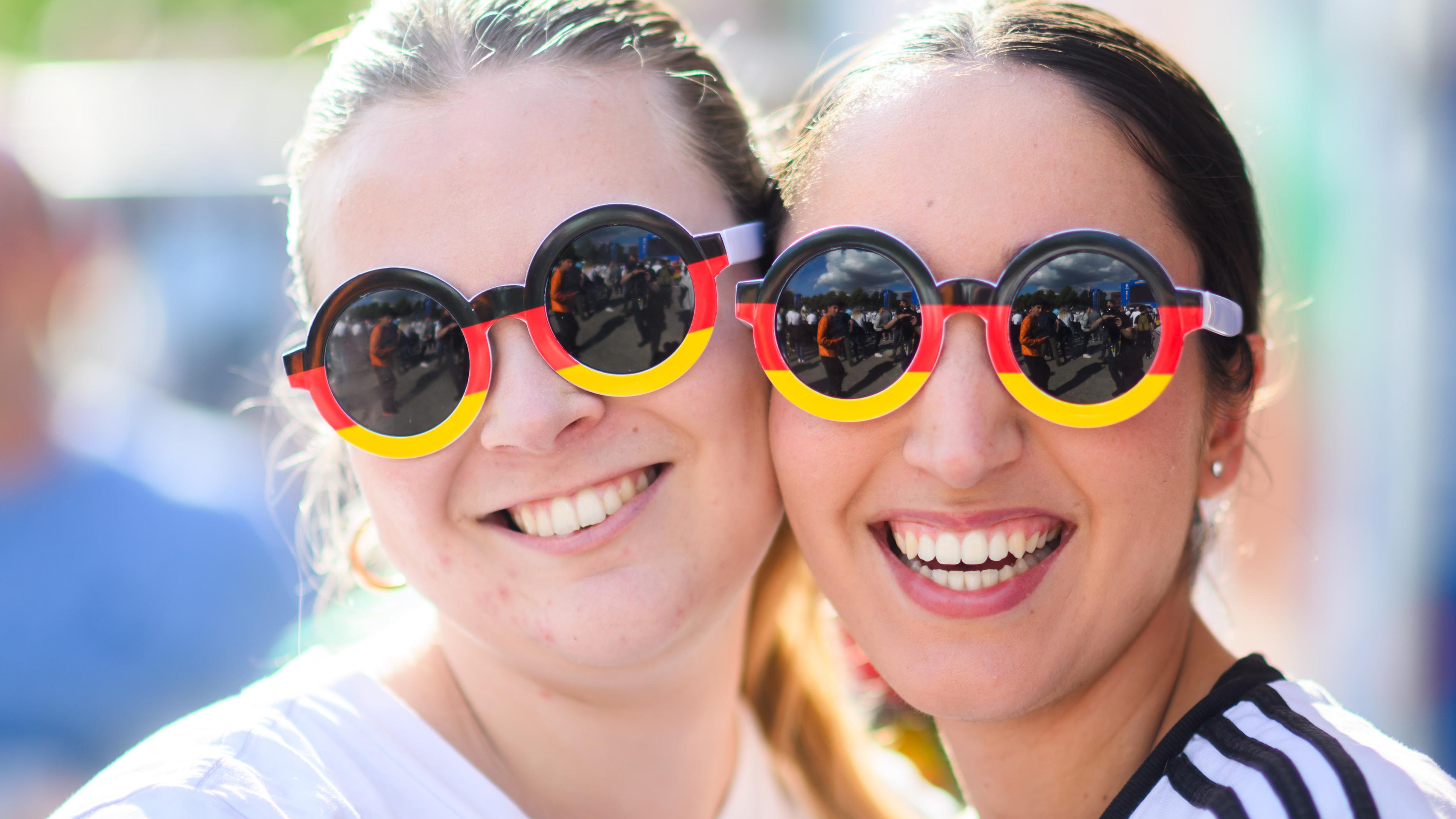 Besucherinnen mit schwarz-rot-goldenen Sonnenbrillen stehen beim Public Viewing im Nordsternpark. 