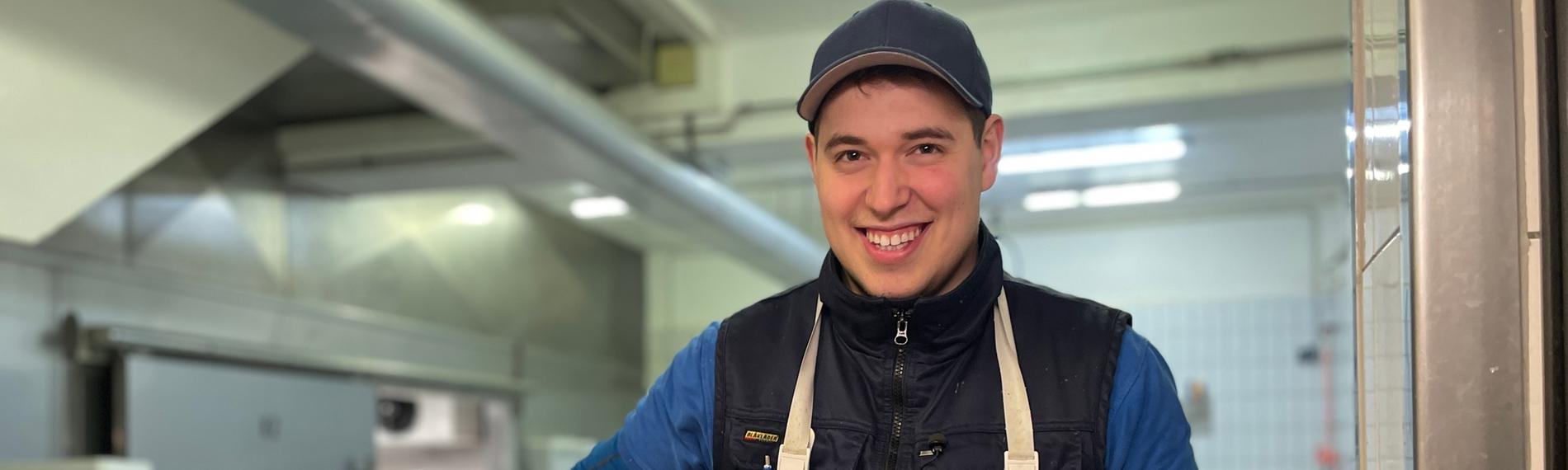 Julian bei der Arbeit, in der einen Hand hält er eine große Schaufel mit Eis. Vor ihm ist eine Plastikwanne mit ganzen Fischen.