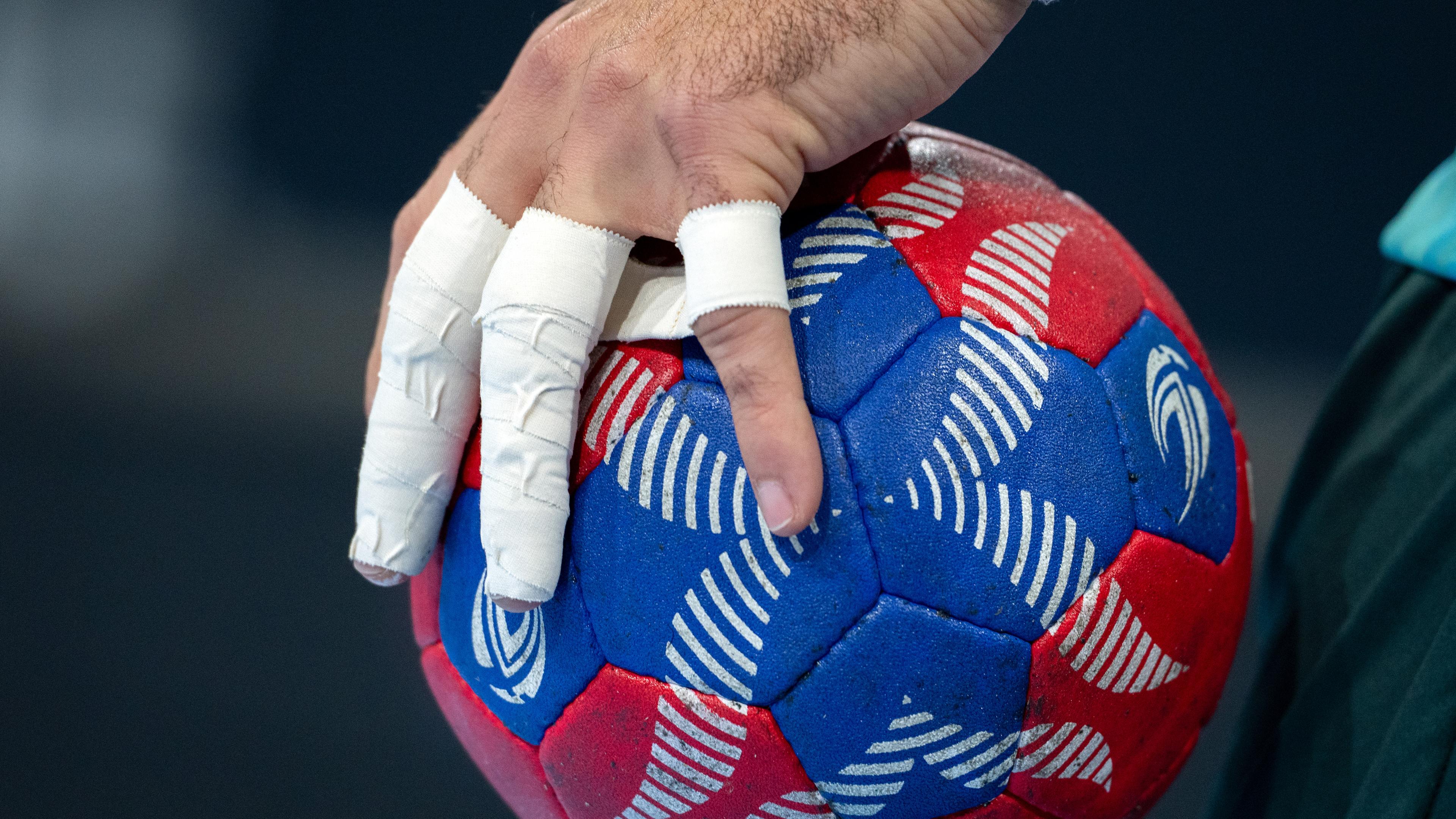 Eine Hand mit bandagierten Fingern hält einen Handball.