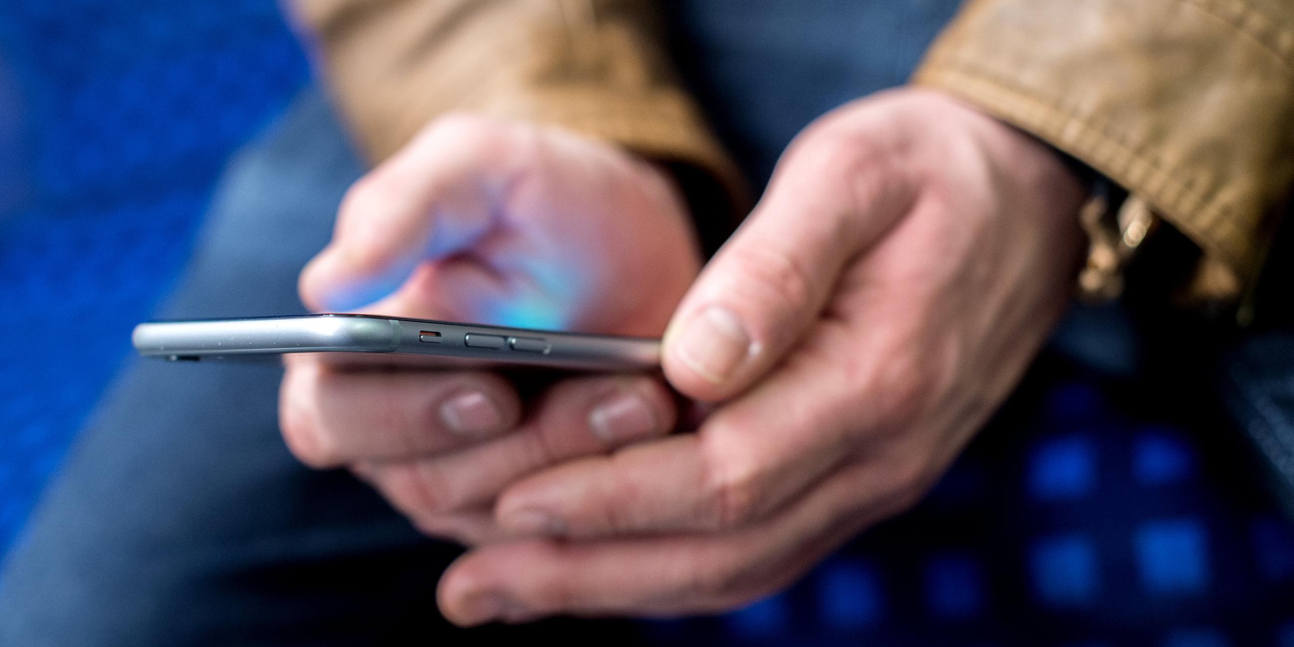 Ein junger Mann sitzt in einer S-Bahn und benutzt dabei sein Smartphone.