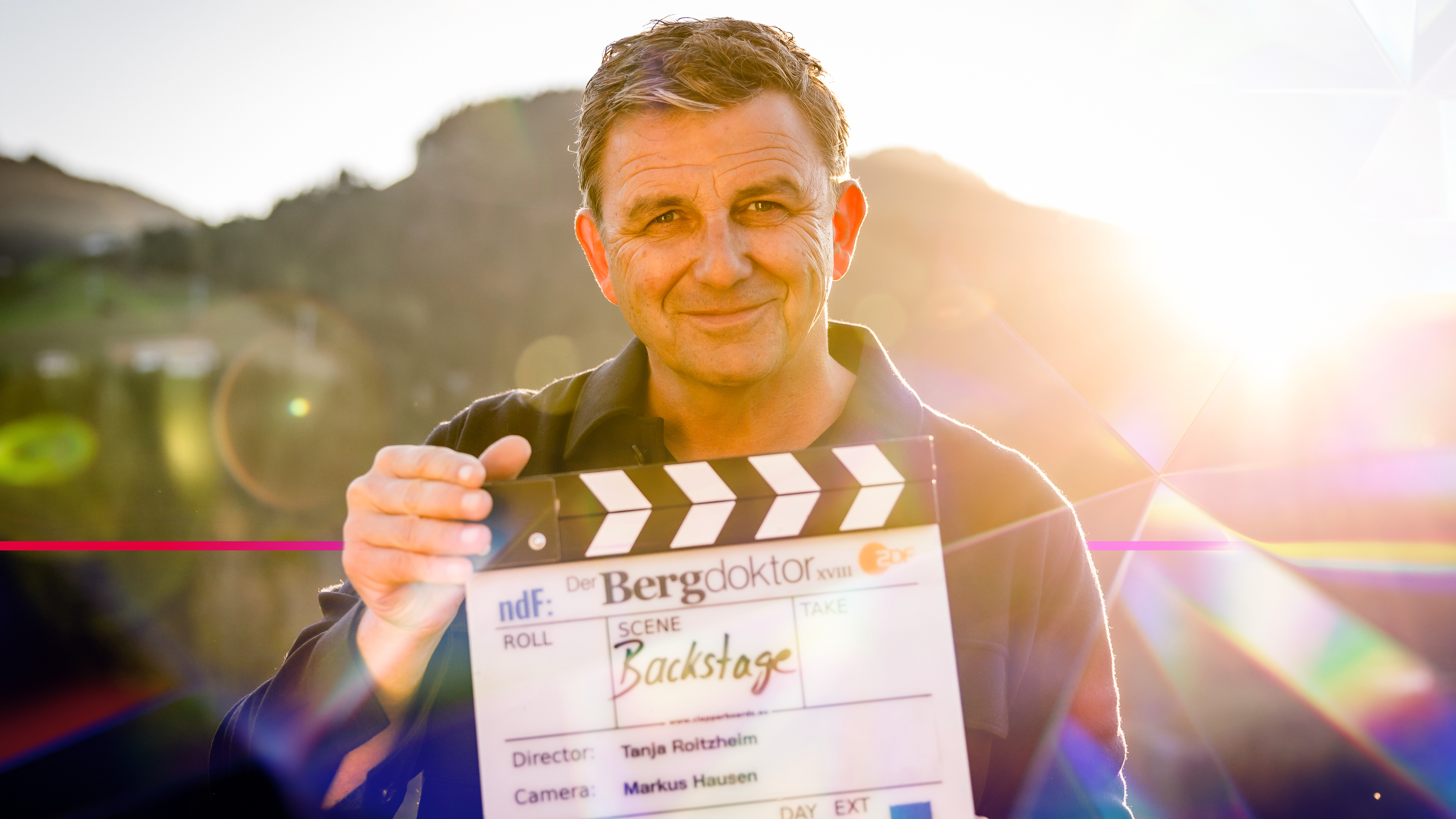 Hans Sigl mit der "Backstage"- Filmklappe am Set von "Der Bergdoktor"