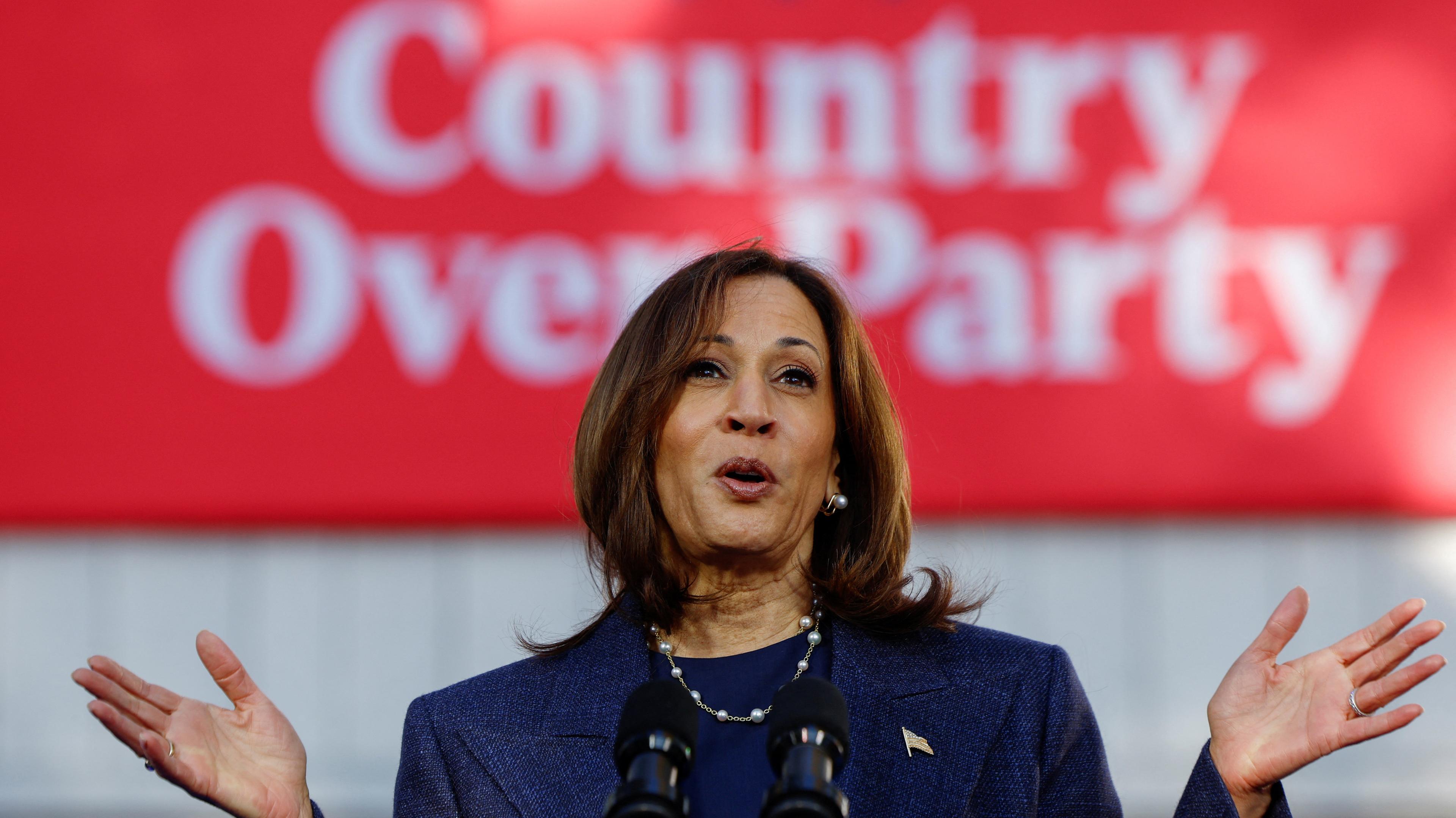 Kamala Harris steht hinter einem Rednerpult und vor einem roten Schild mit der Aufschrift "Country Over Party".