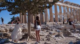 Una donna beve acqua davanti all'antico tempio del Partenone in una giornata calda e ventosa il 16 luglio 2024 sulla collina dell'Acropoli di Atene.