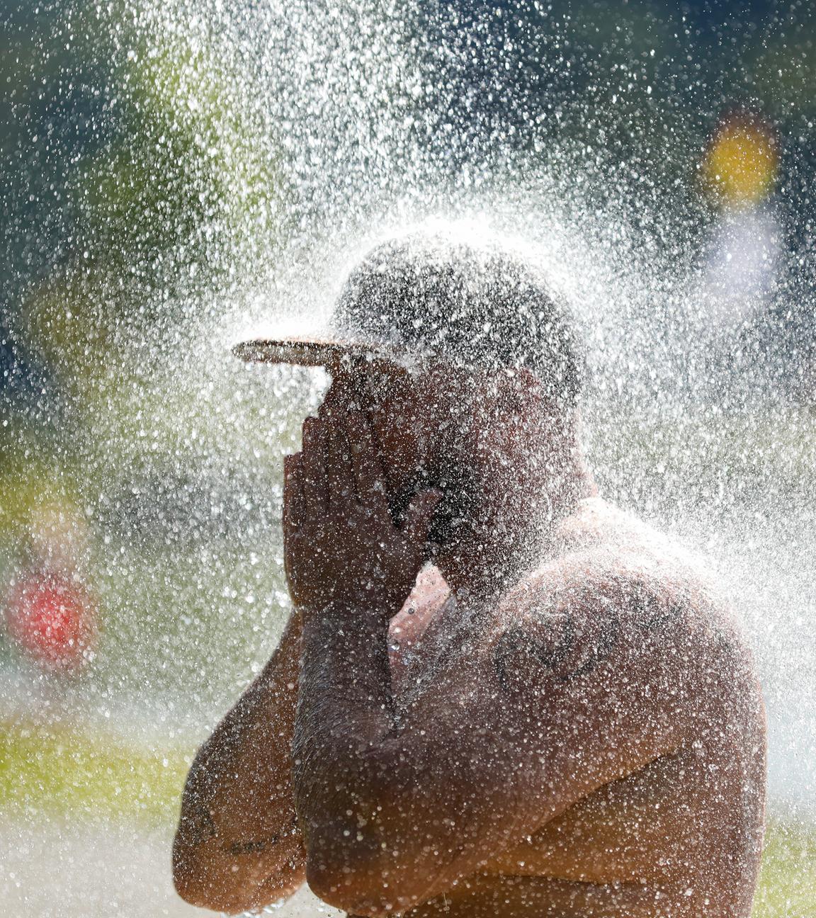 Ein Mann erfrischt sich an einem Badesee unter einer kalten Dusche.