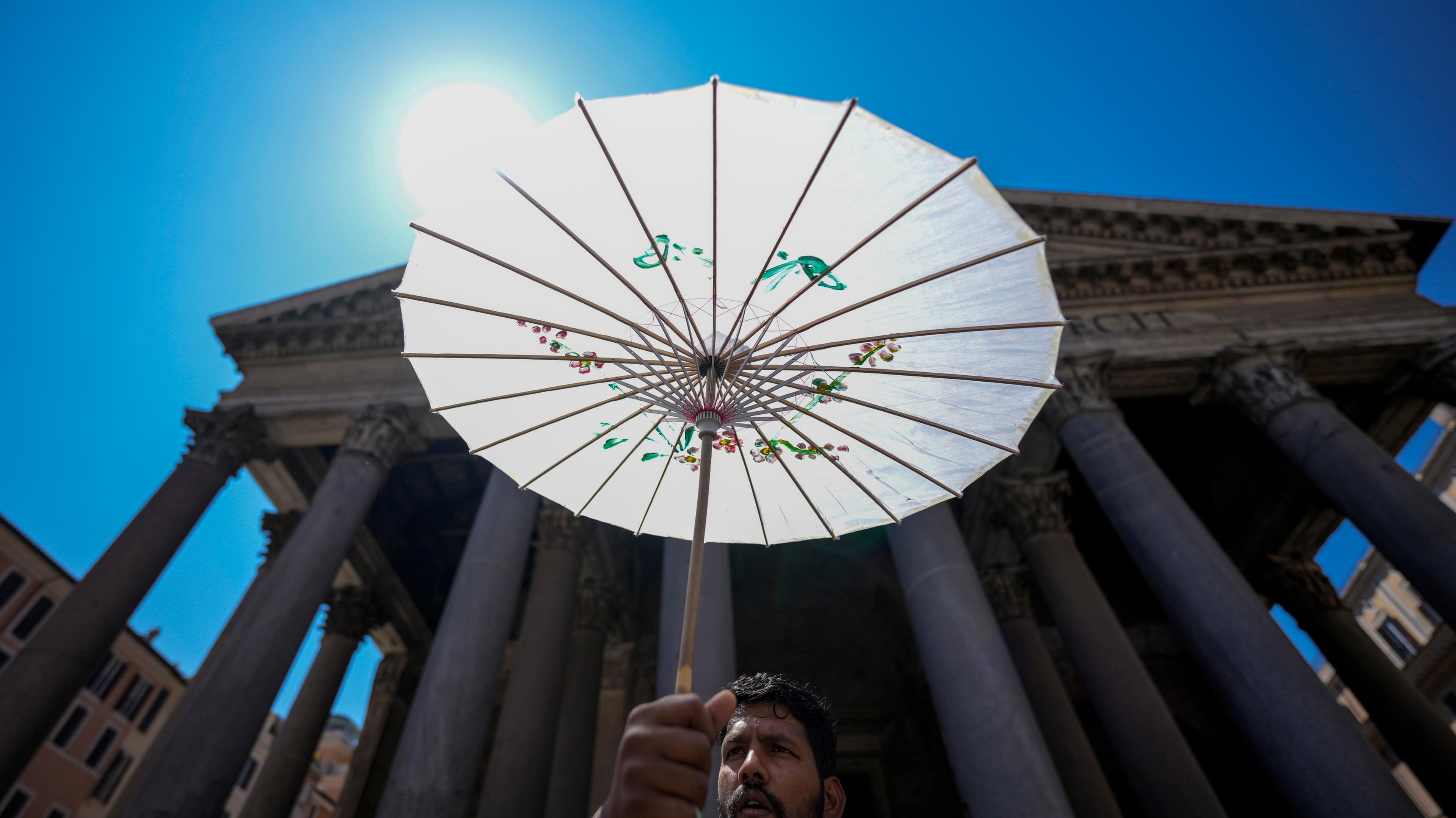 11.07.2024, Italien, Rom: Ein Mann schützt sich während einer Hitzewelle mit einem Papierschirm vor dem Pantheon.