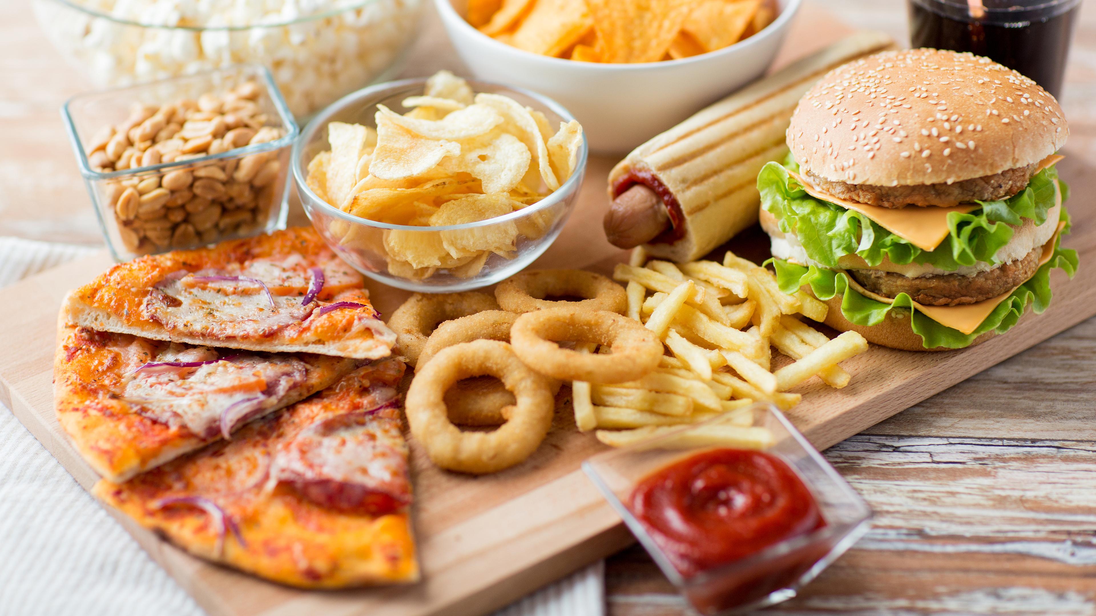 Verschiedene Fast Food Gerichte liegen auf einem Tisch, darunter Chips, Pizza, Pommes und Burger.