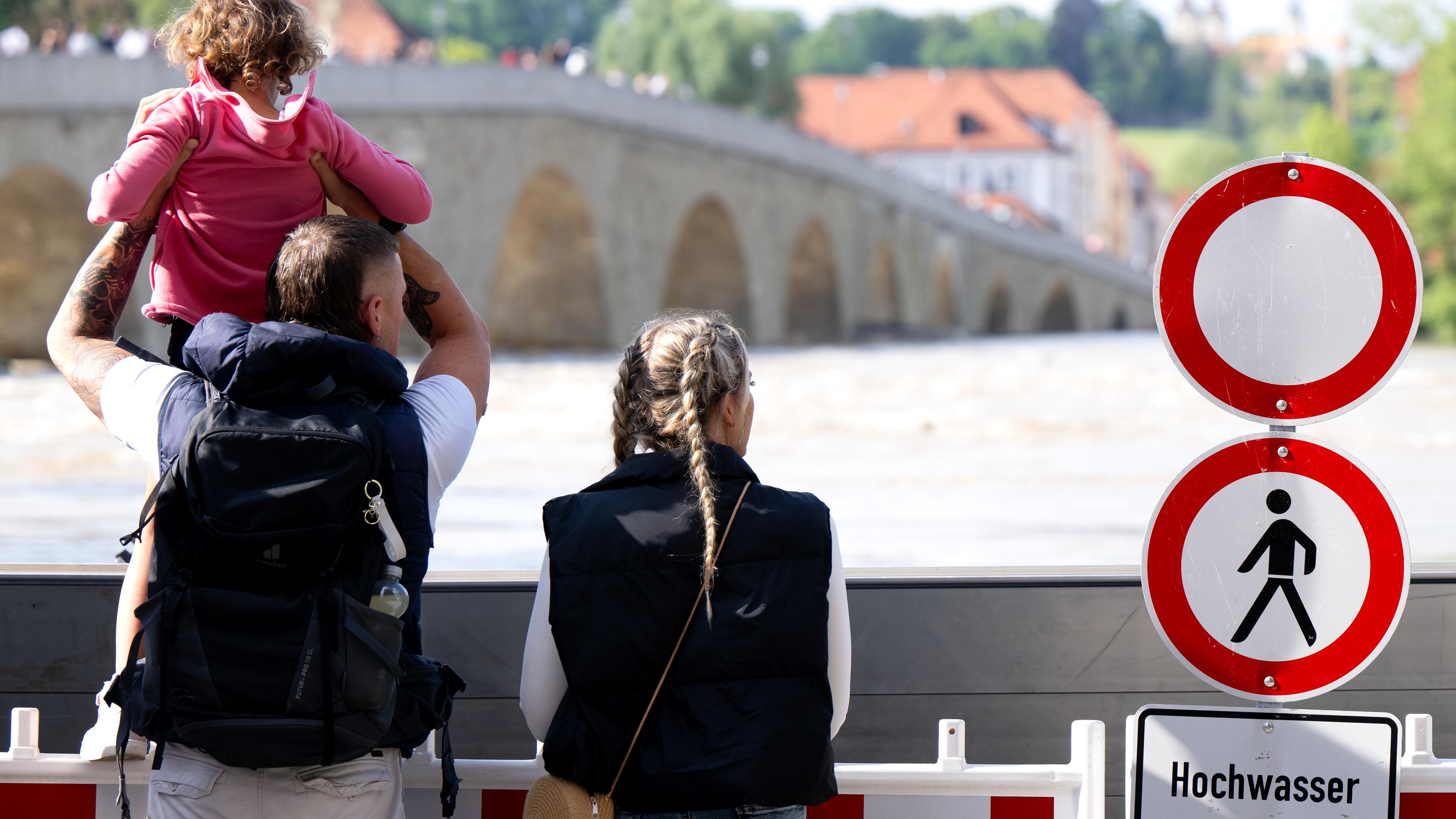 04.06.2024, Bayern, Regensburg: Menschen schauen sich in der Altstadt am Donauufer hinter einer Schutzwand das Hochwasser an. Seit Tagen kämpfen die Helfer in Bayern gegen die Flut und ihre Folgen.