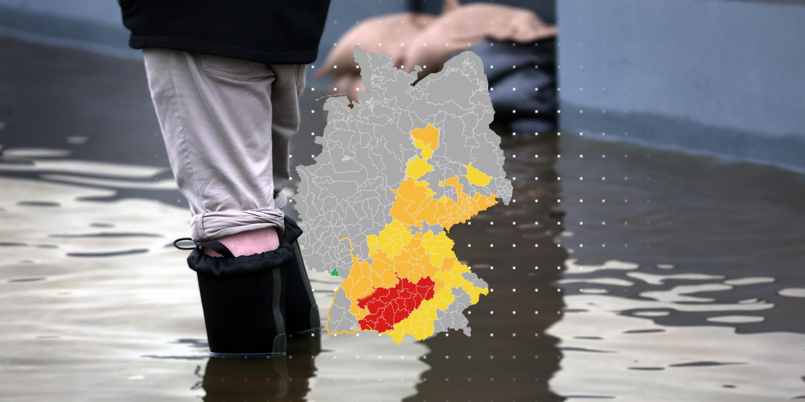 Die Montage zeigt eine Deutschland-Karte, auf der verschiedene Hochwasser-Warnstufen zu sehen sind. Im Hintergrund sind Sandsäcke und die Beine einer Person in Gummistiefeln zu sehen, Wasser steht ihr bis zu den Waden.
