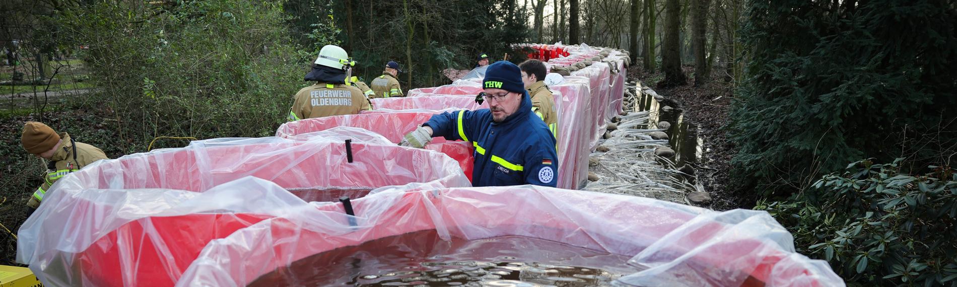 Mitarbeiter von THW und der Feuerwehr Oldenburg befüllen Elemente eines mobilen Notdeichs mit Wasser am 03.01.2024.