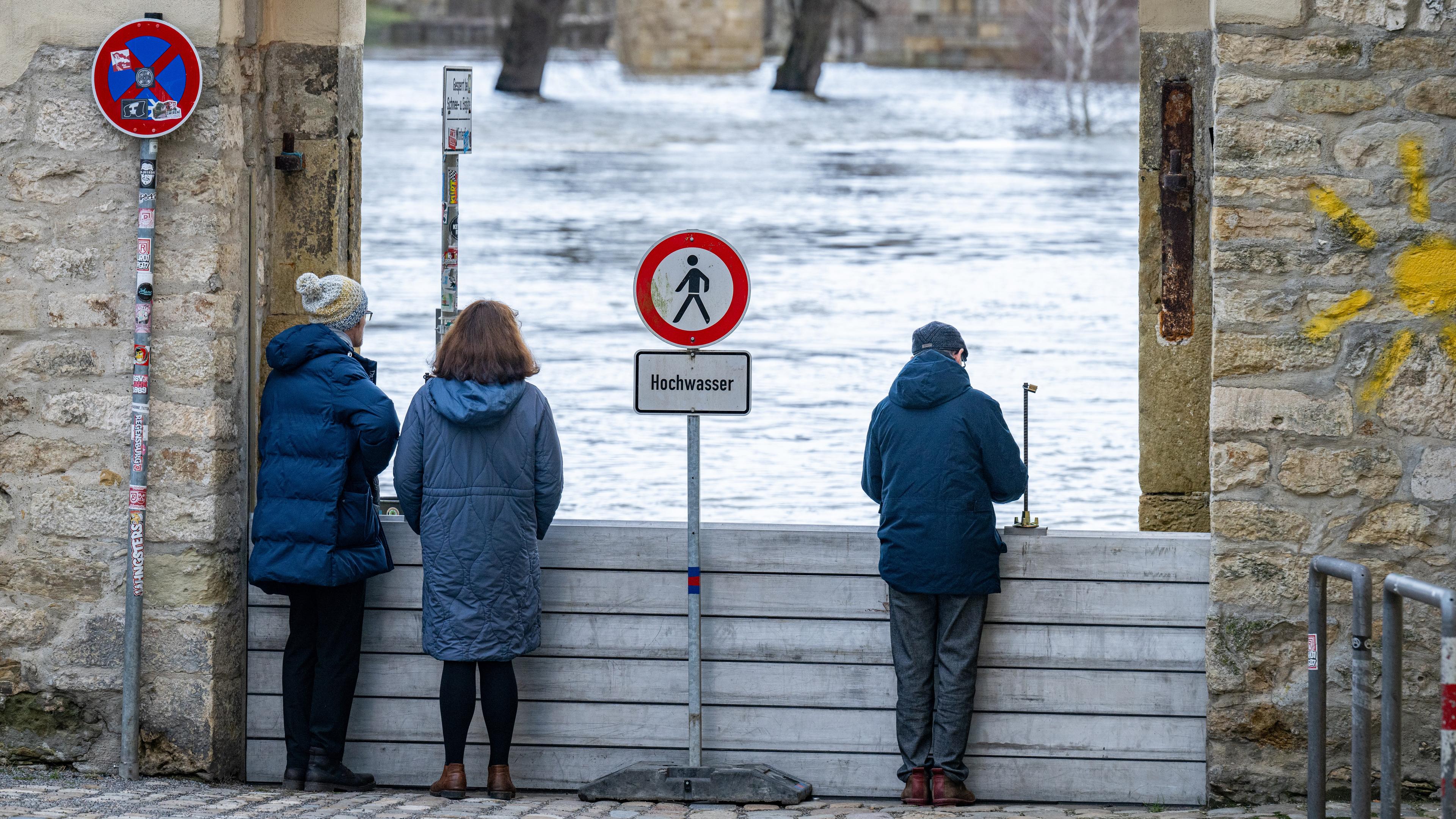 Drei Menschen beobachten von einer Brücke aus das Hochwasser in der Donau