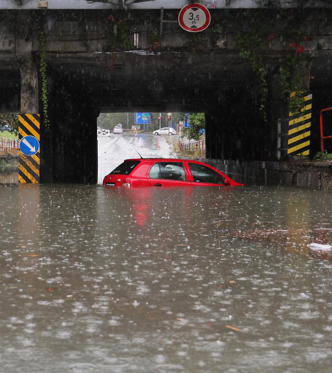  Ein Auto steht unter einer Bahnlinie in einer überfluteten Unterführung im Wasser