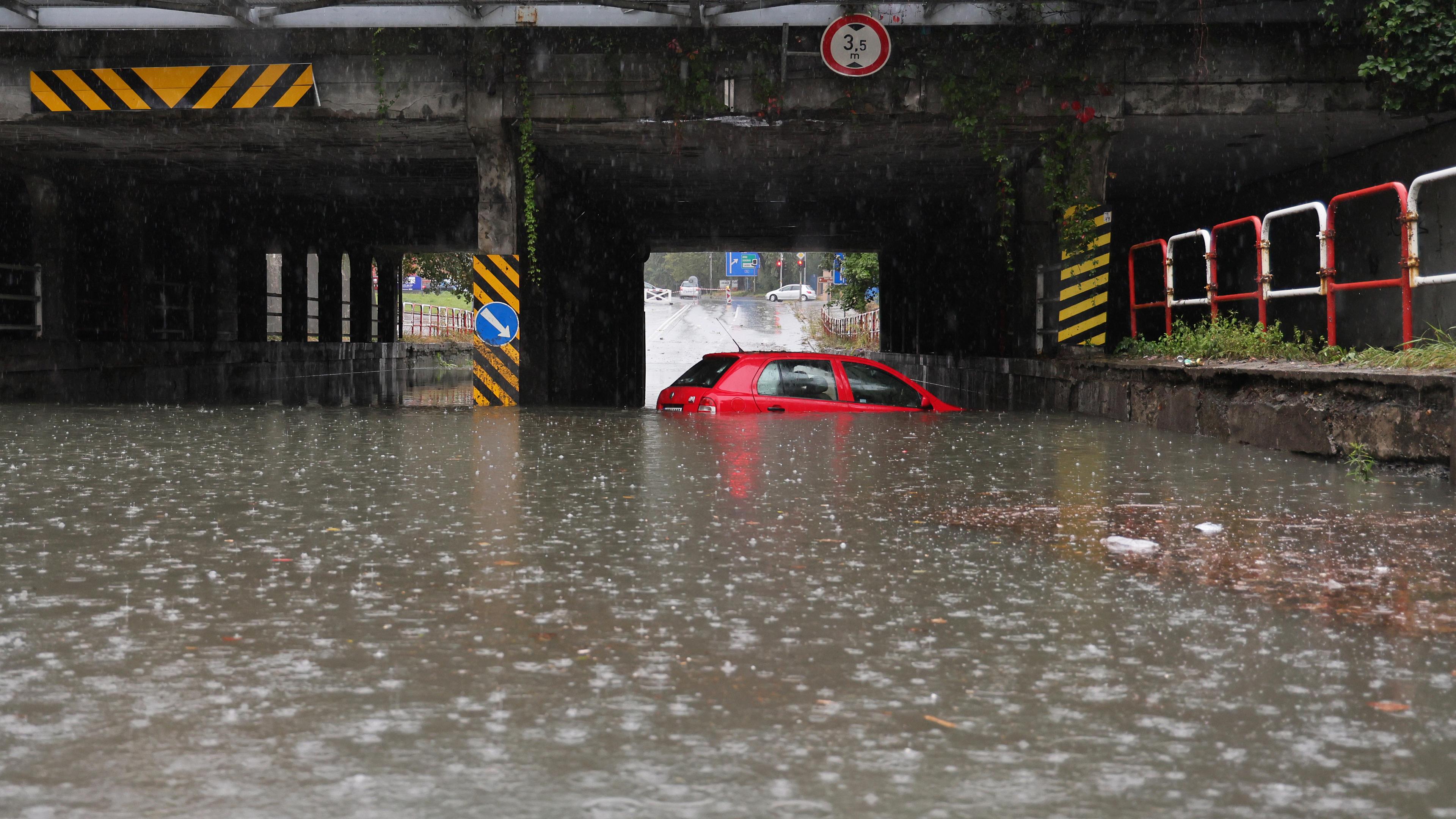  Ein Auto steht unter einer Bahnlinie in einer überfluteten Unterführung im Wasser