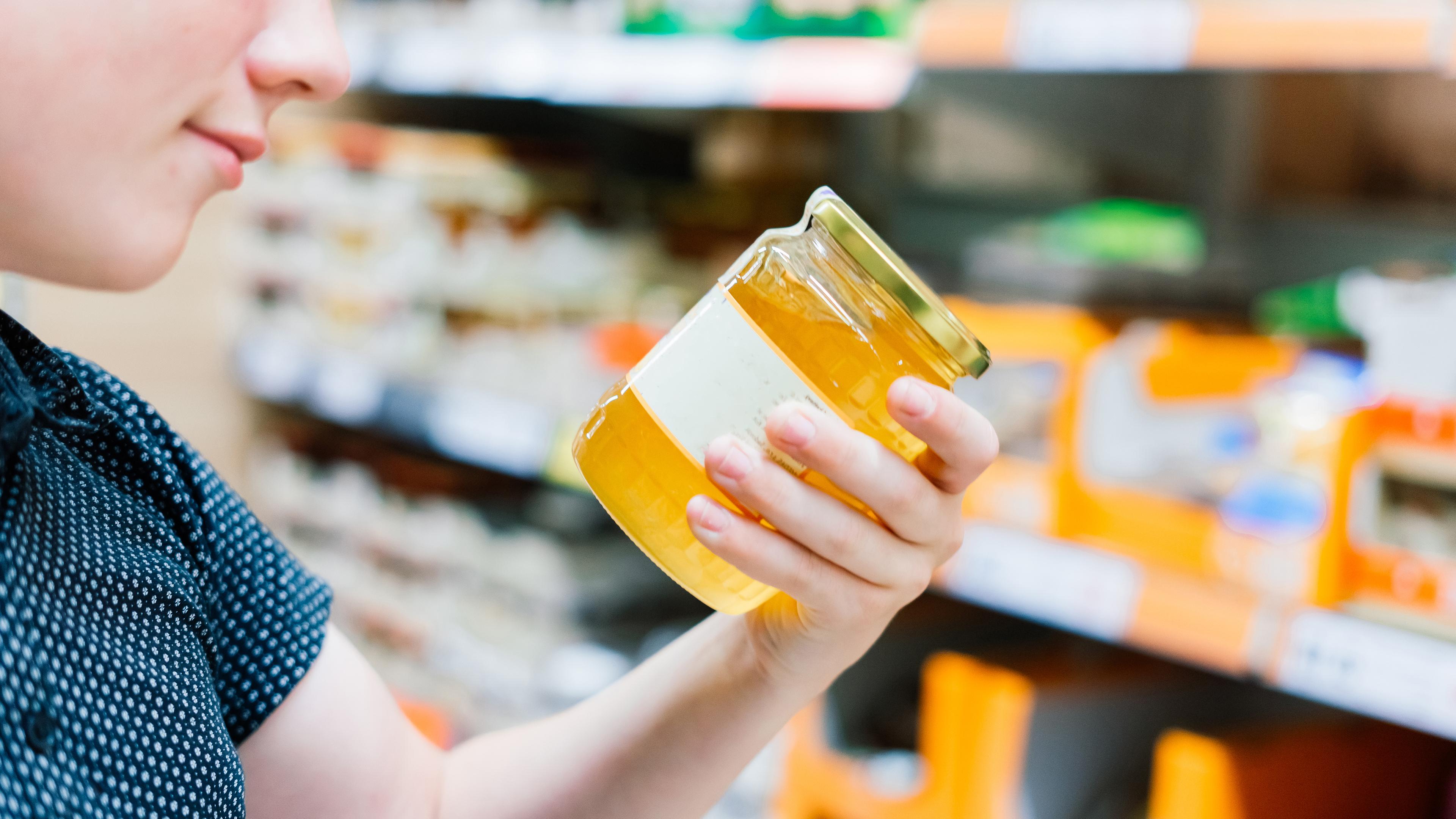 Ein Junge im Supermarkt hält ein Glas Honig