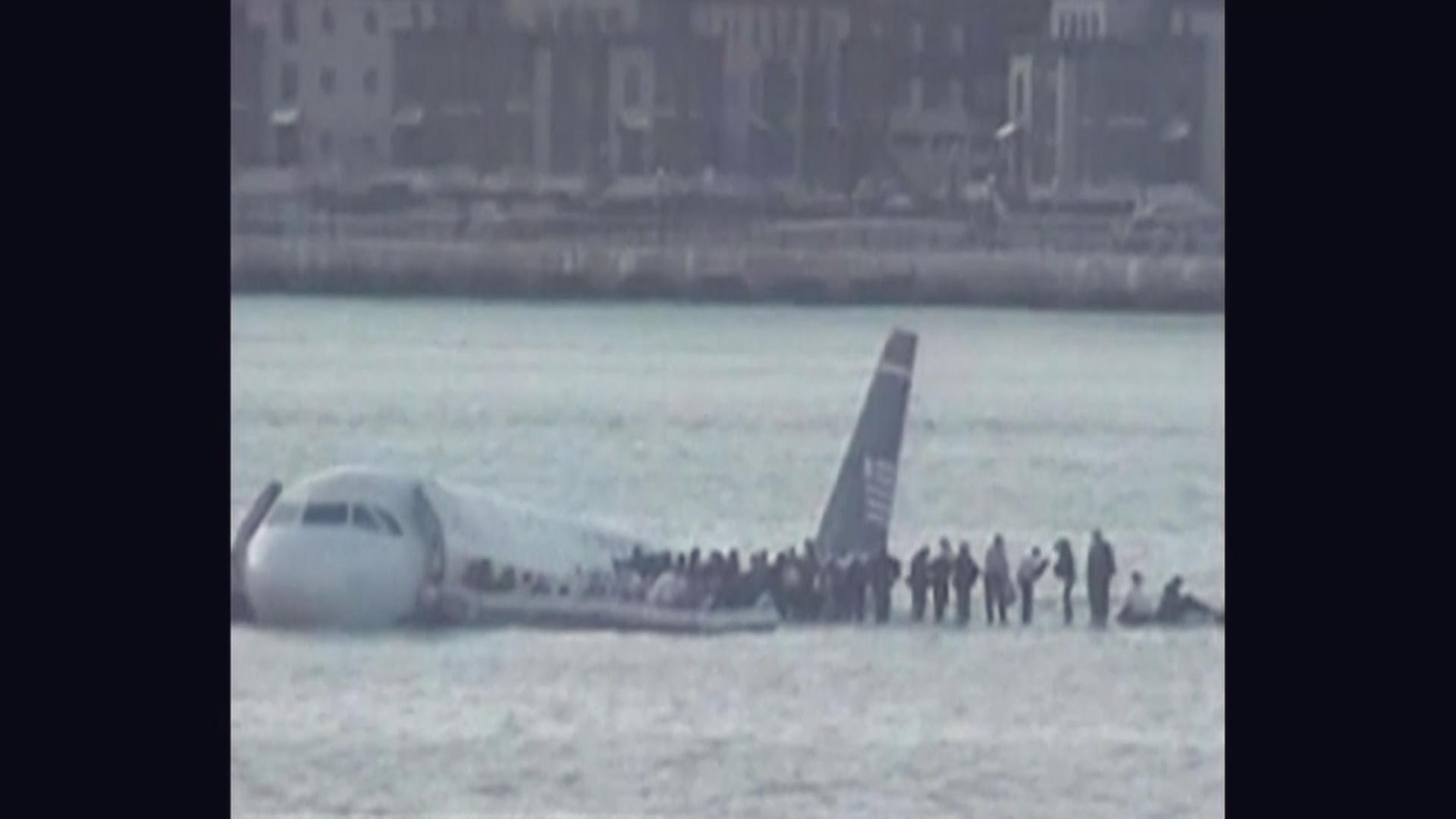 Ein Flugzeug schwimmt im Hudson River. Personen steigen durch die Notausgänge aus. 