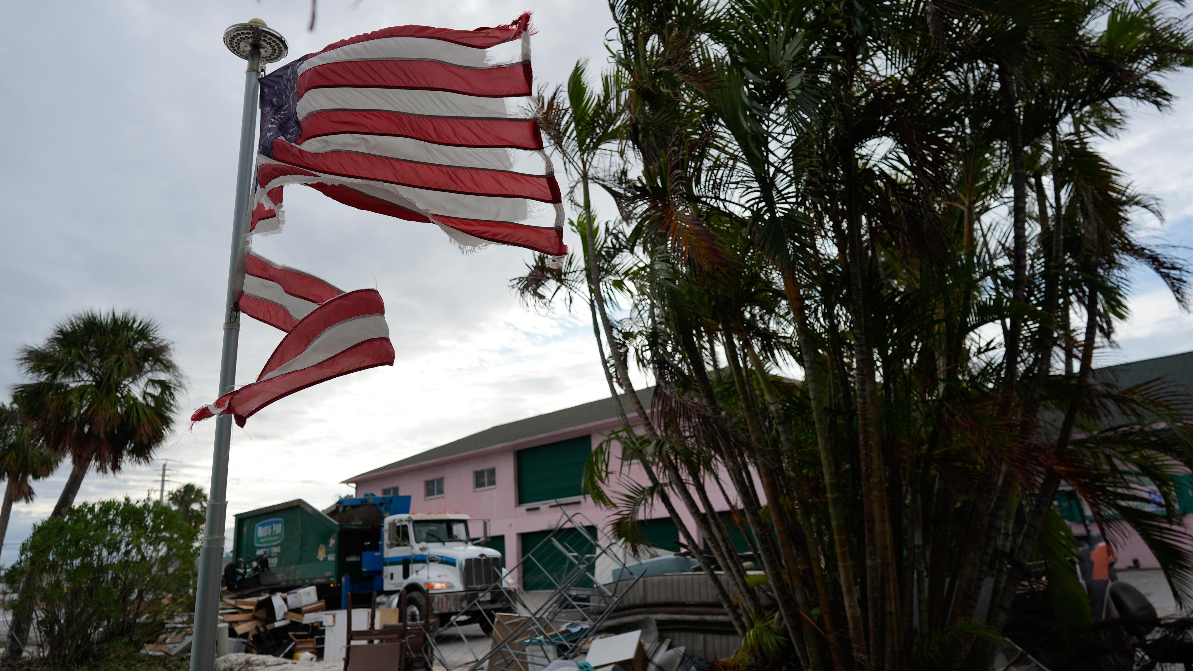 Zerrissene US-Flagge im Hurrikansturm in Florida vor Palmen.