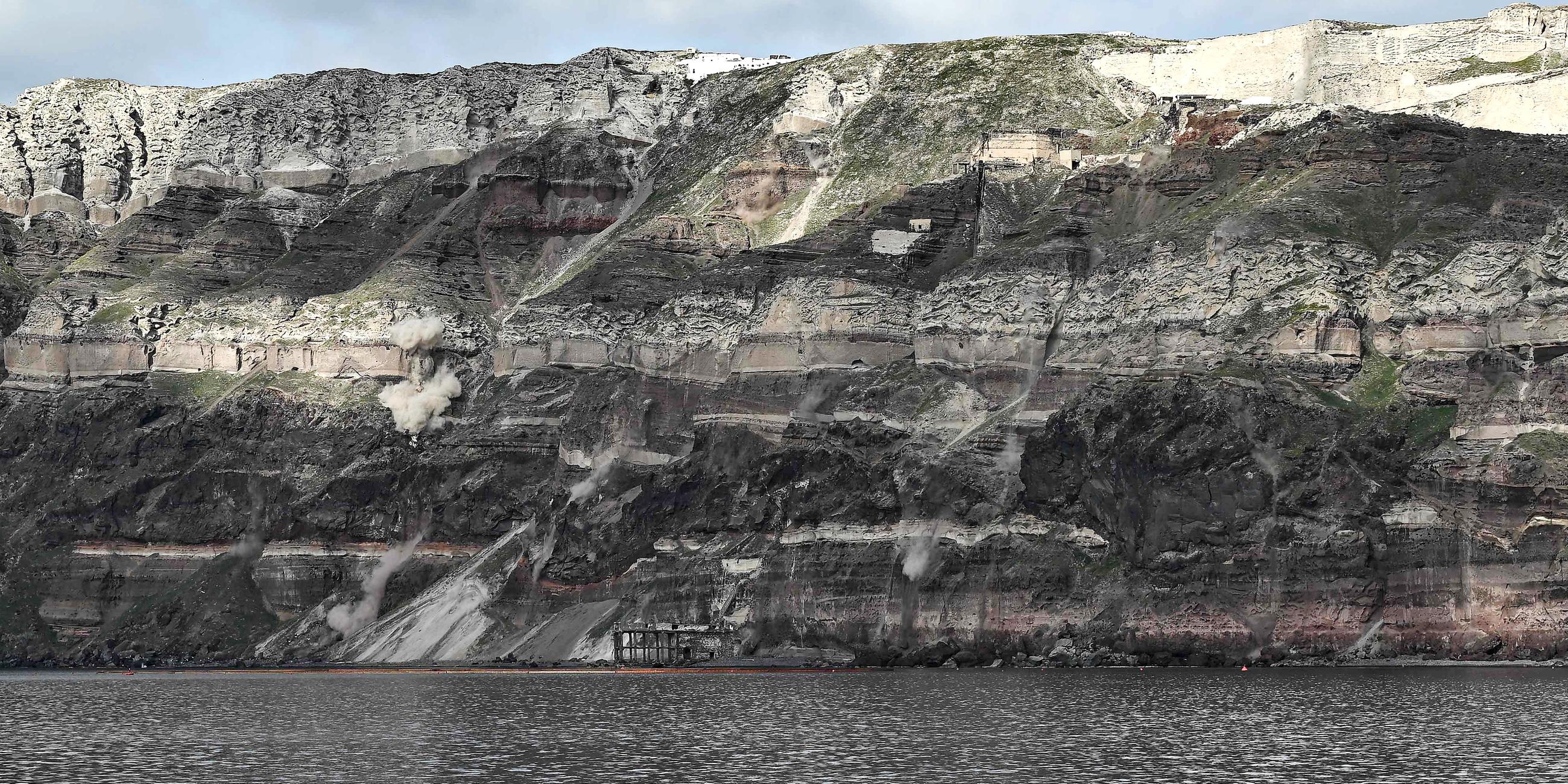 Felsstürze durch Erdrutsche, die durch Erdbeben verursacht wurden, wirbeln am 03.02.2025 Staubwolken entlang der Felswand auf der griechischen Insel Santorini auf