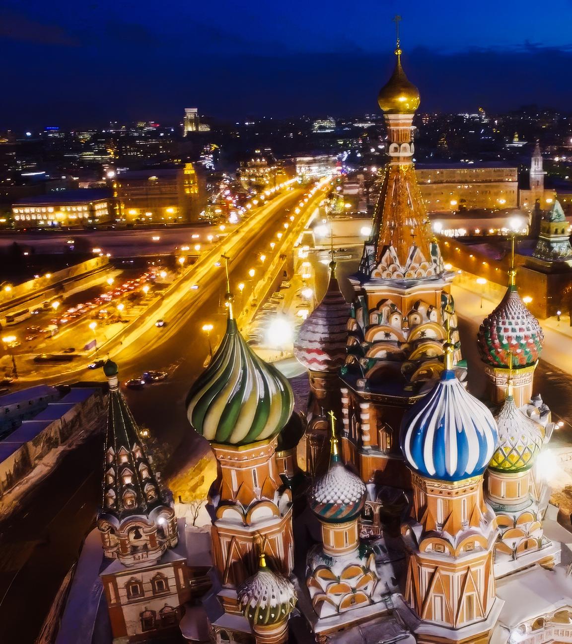 Luftbild: Moskau bei Nacht mit beleuchteten Straßen und einer Kathedrale mit bunten Türmen im Vordergrund