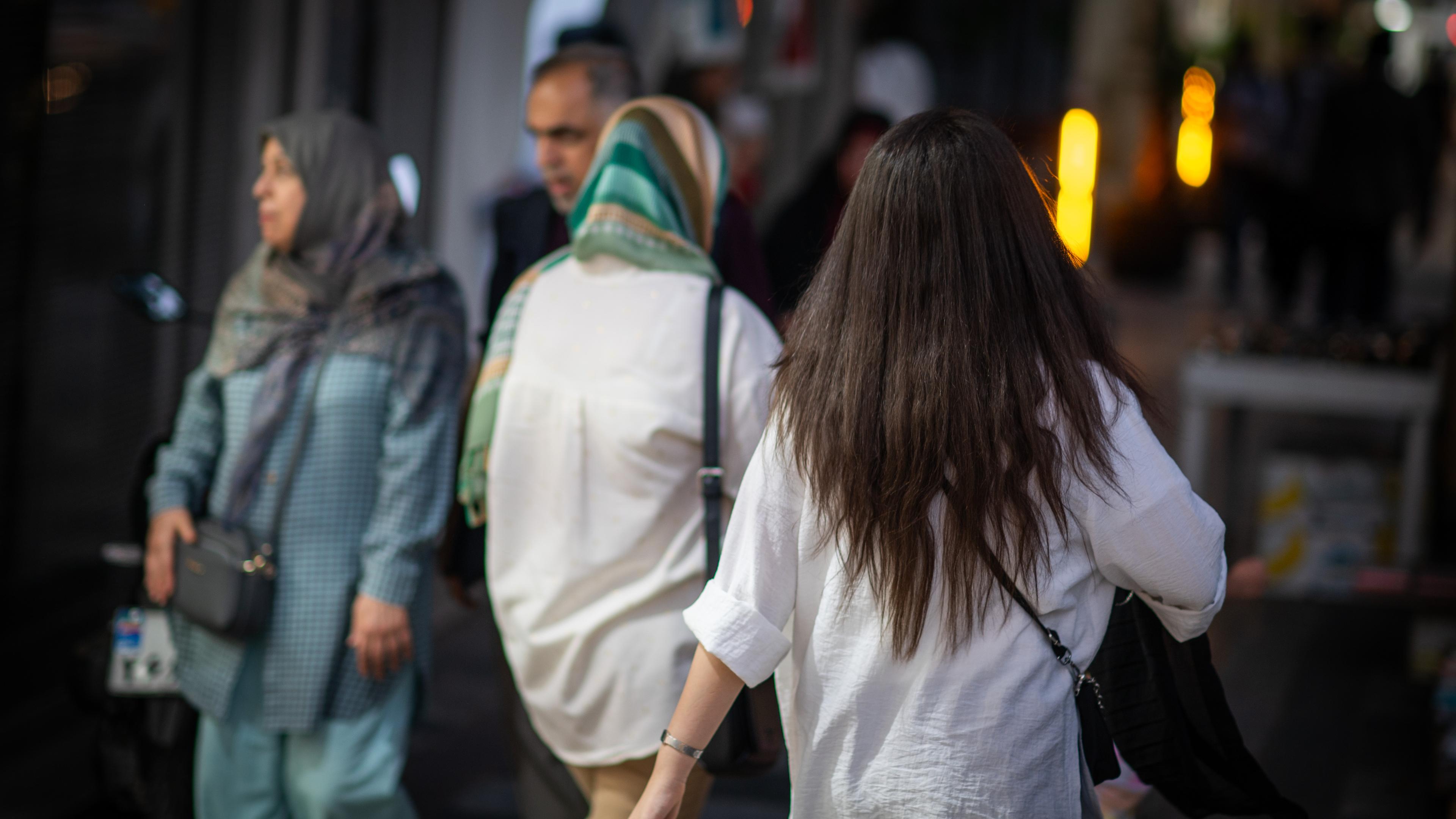 Eine Frau läuft in Teheran mit offenen Haaren am Abend eine Straße entlang.