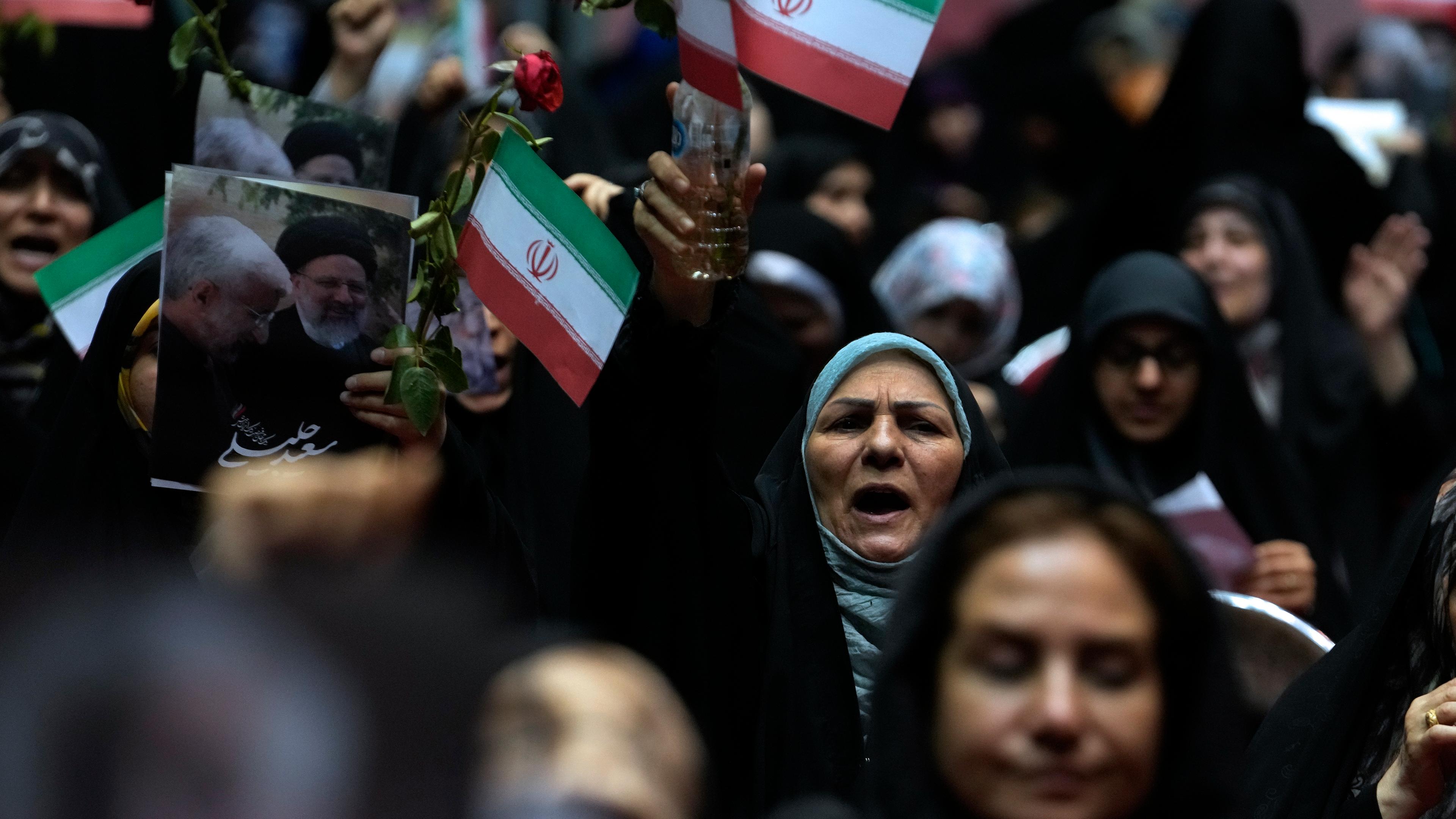 Menschen auf einer Wahlkampfveranstaltung halten iranische Fahnen hoch.
