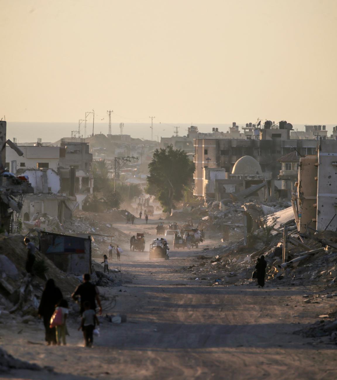 Menschen gehen an zerstörten Gebäuden im Gazastreifen vorbei.