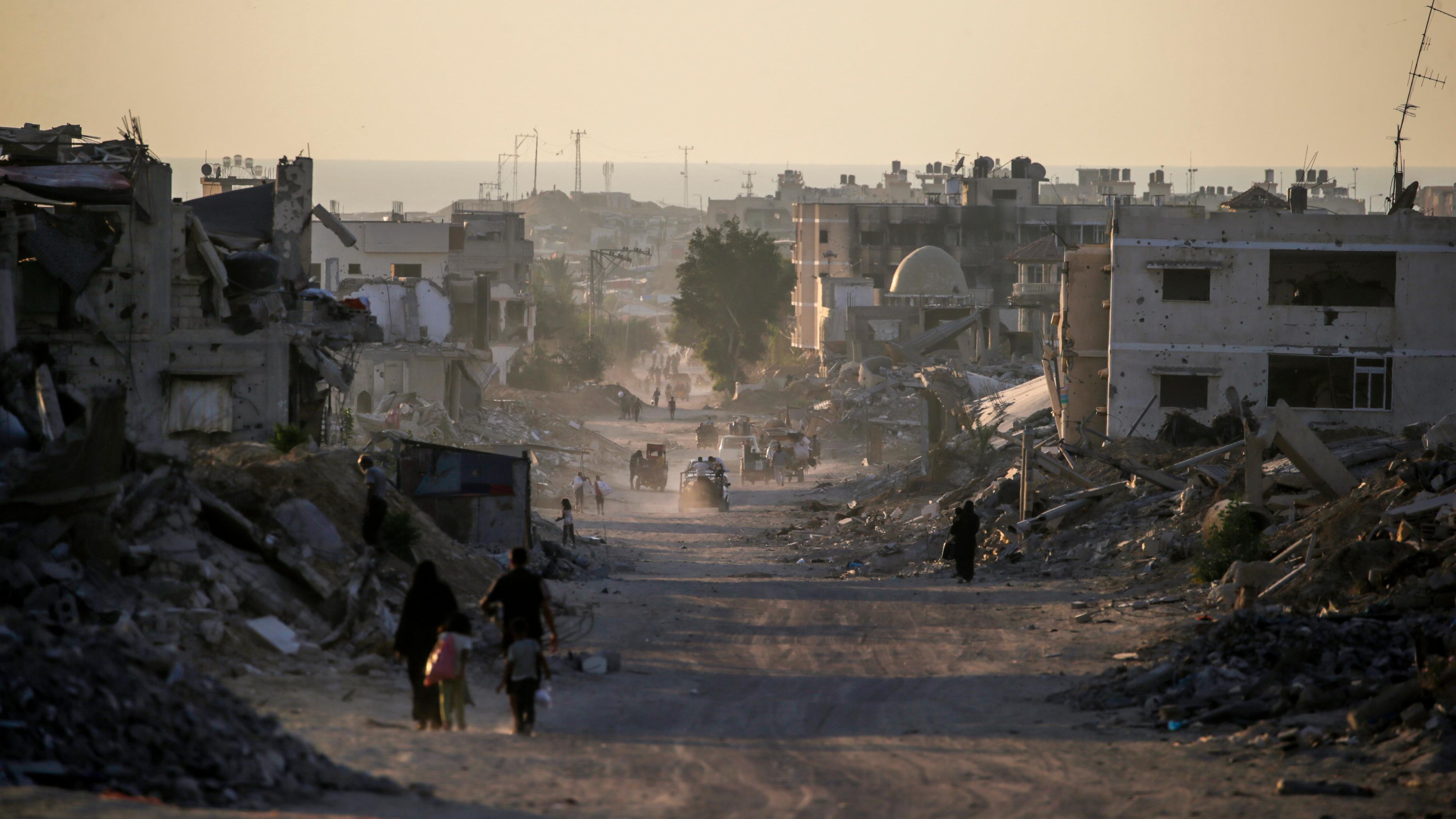 Menschen gehen an zerstörten Gebäuden im Gazastreifen vorbei.