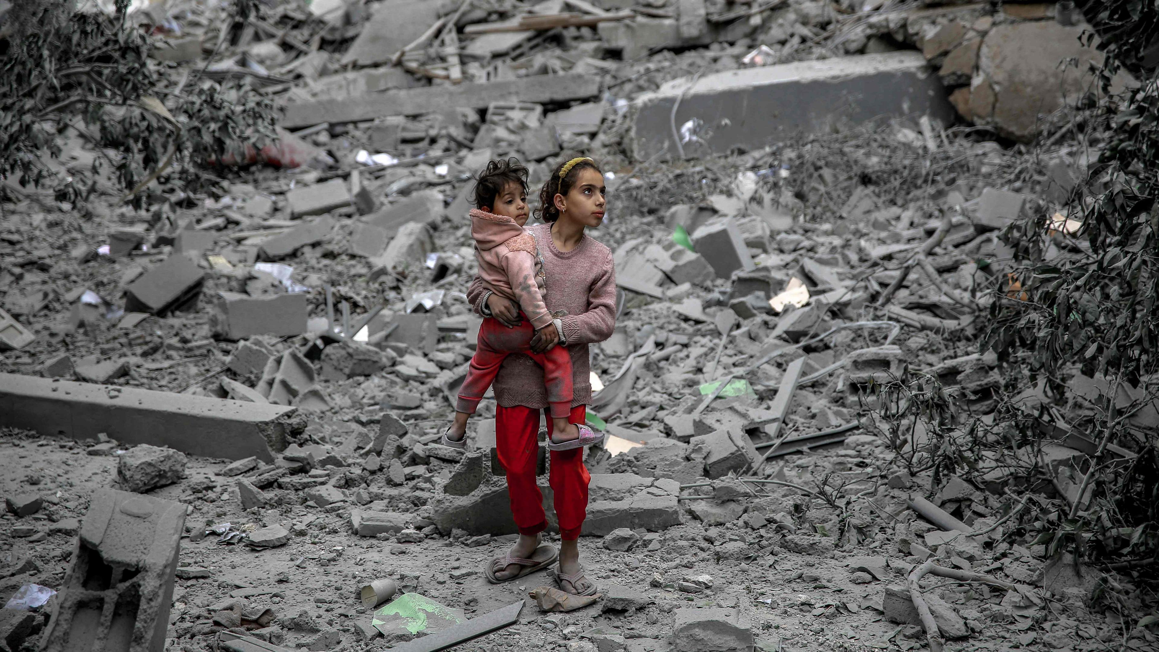 A Palestinian girl carries a child through the rubble of houses destroyed by Israeli bombardment in Gaza City on March 3, 2024, amid the ongoing conflict between Israel and the Hamas movement. 