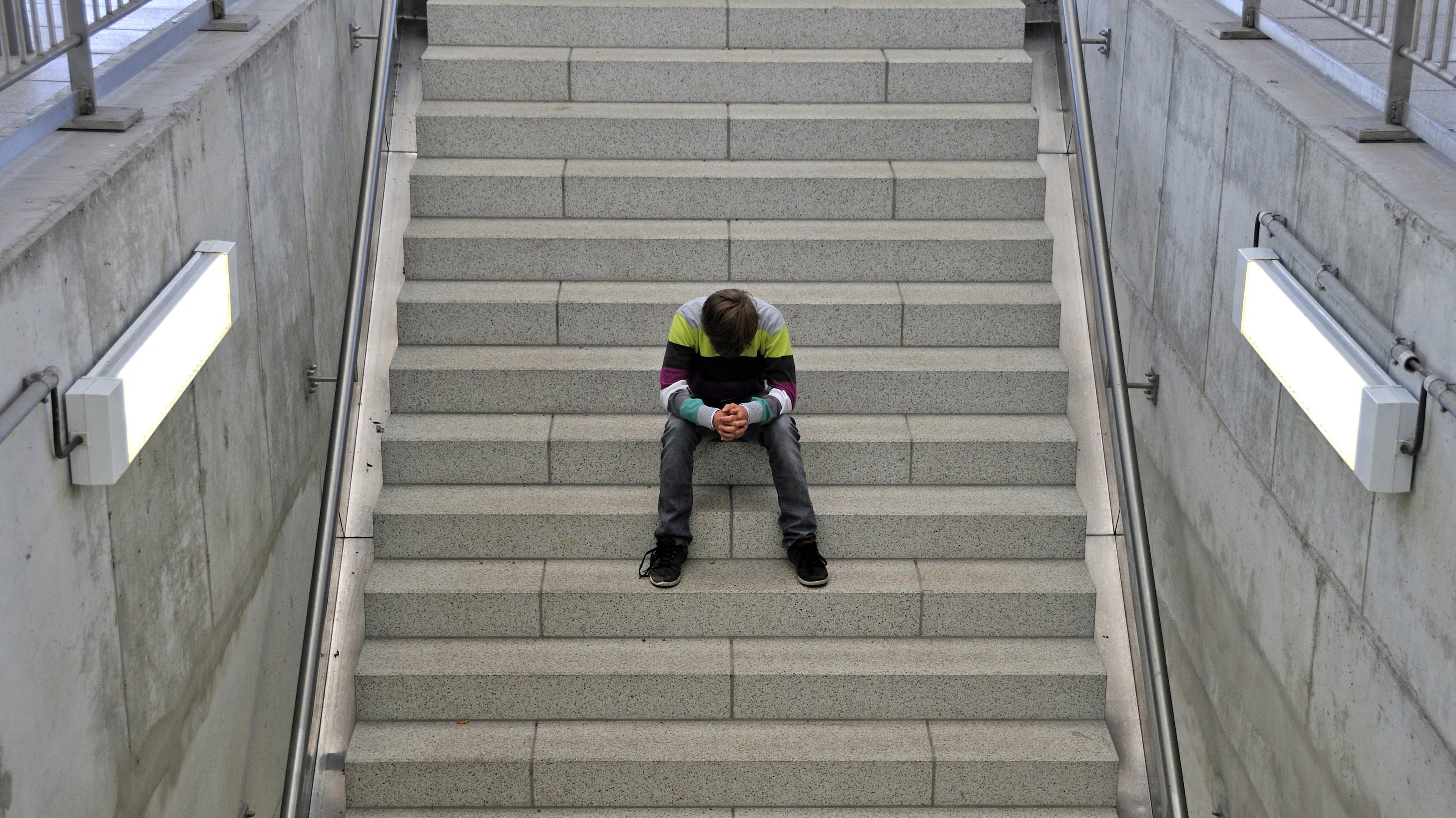 Ein einsamer elfjähriger Junge sitzt auf einer Treppe am Bahnhof.