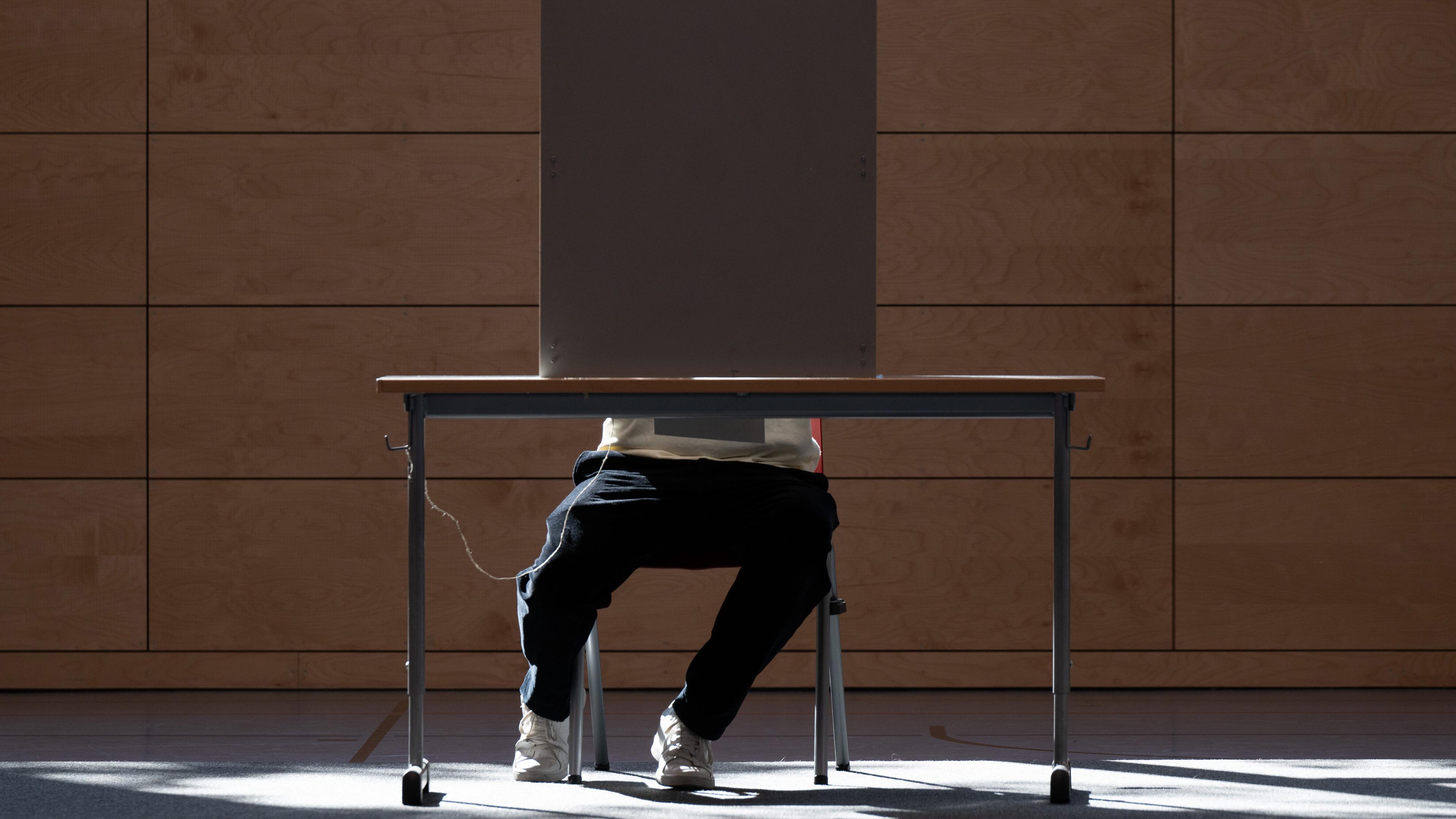 Ein junger Wähler sitzt für die Stimmabgabe zur Landtagswahl in Sachsen in einer Sporthalle in einer Wahlkabine.