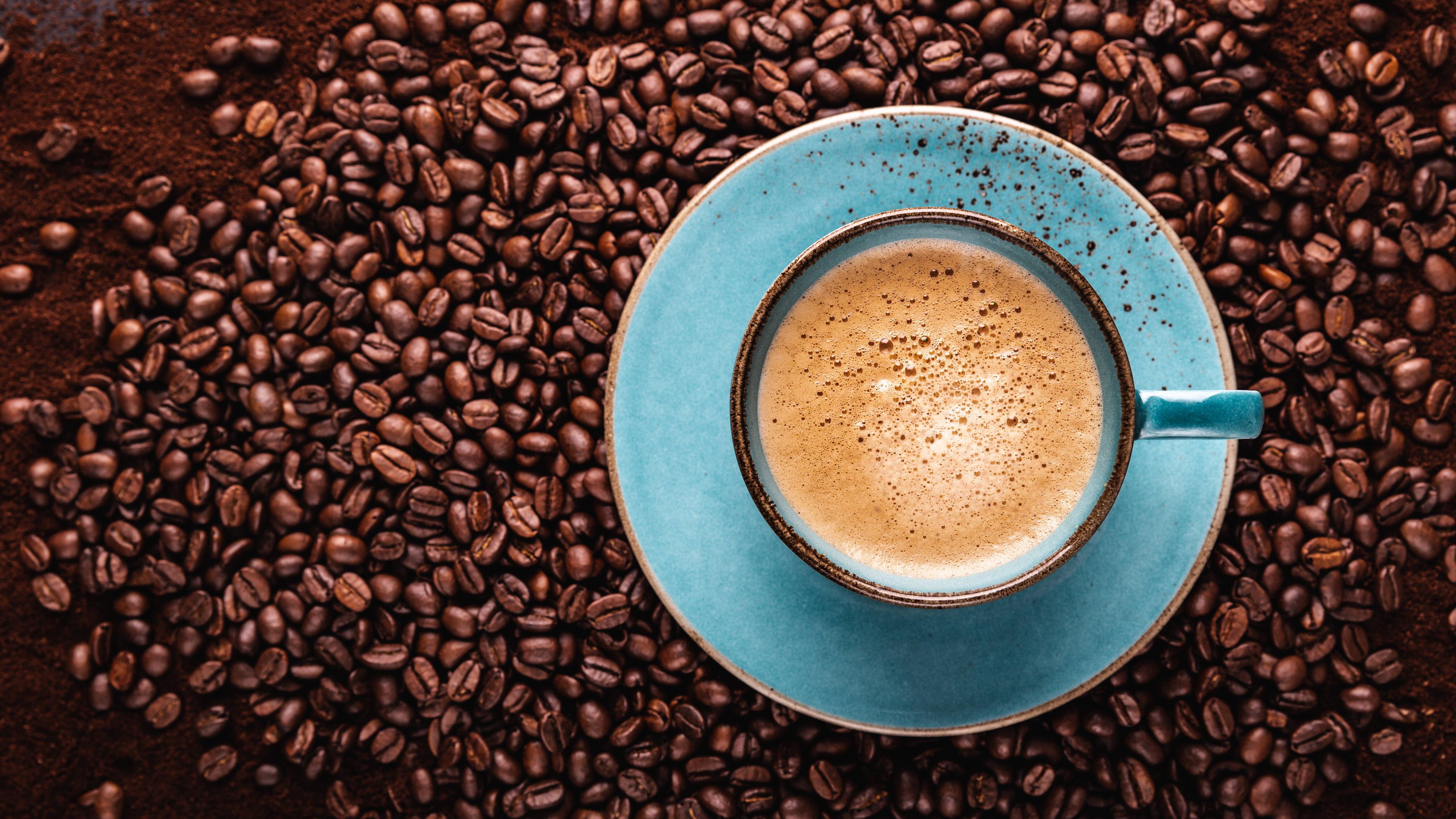 Eine blaue Kaffetasse mit Kaffee gefüllt steht auf einem Tisch mit Kaffeebohnen.