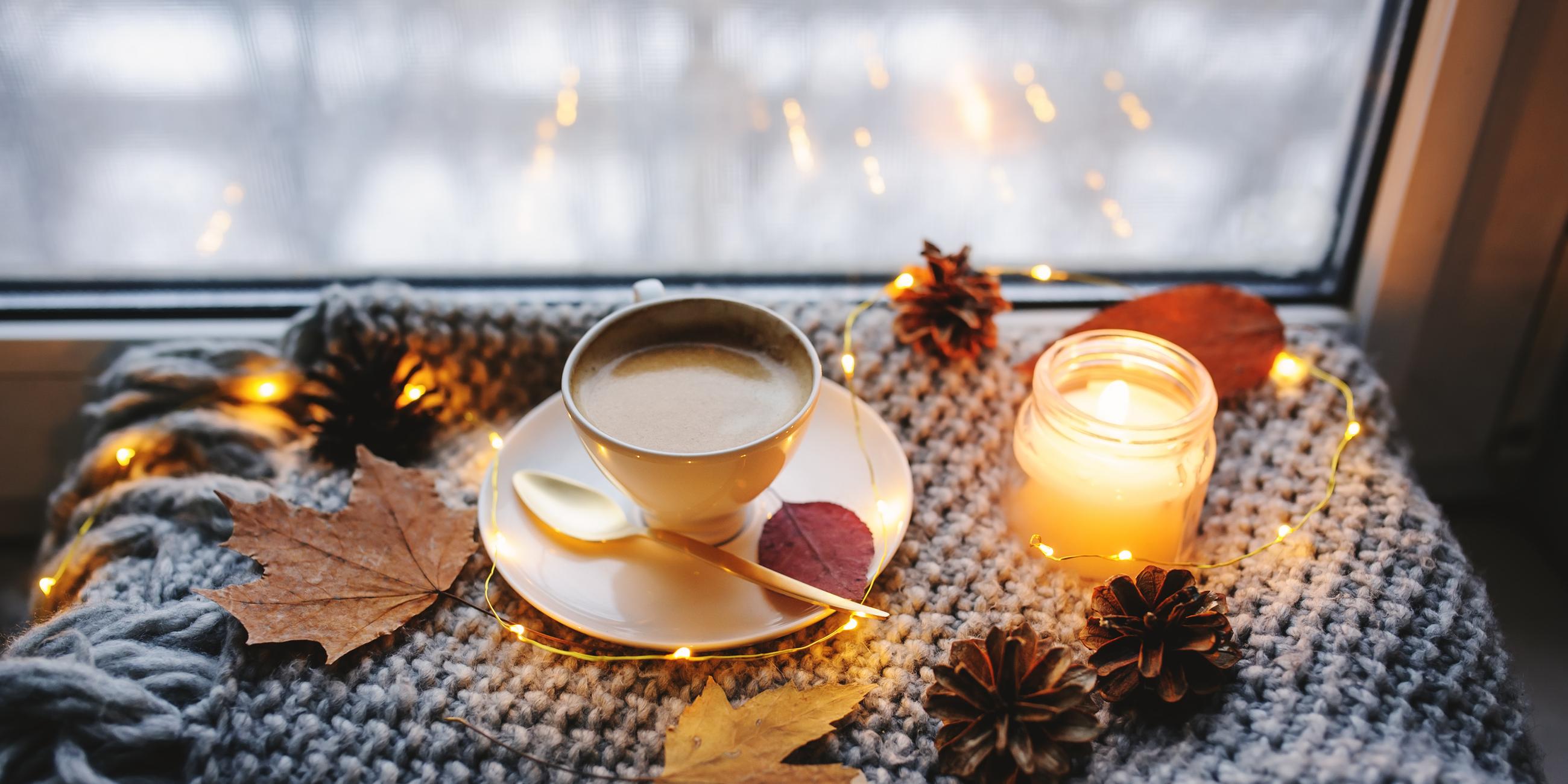 Eine Kerze, eine Tasse Kaffee und Herbstdekoration auf einer Fensterbank.