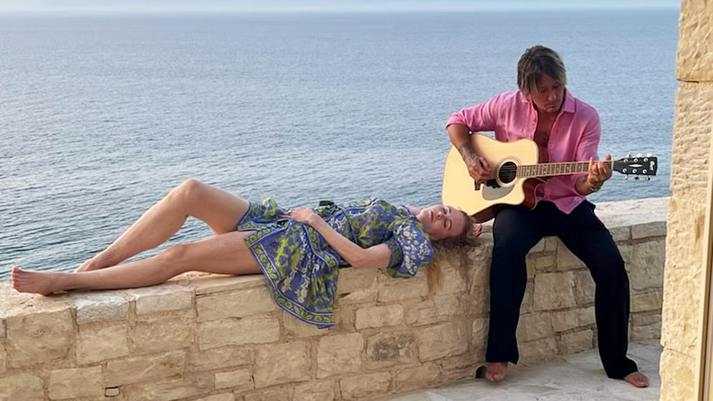 Nicole Kidman liegt auf einer Mauer; Keith Urban hält eine Gitarre; hinter ihnen ist Meer zu sehen.