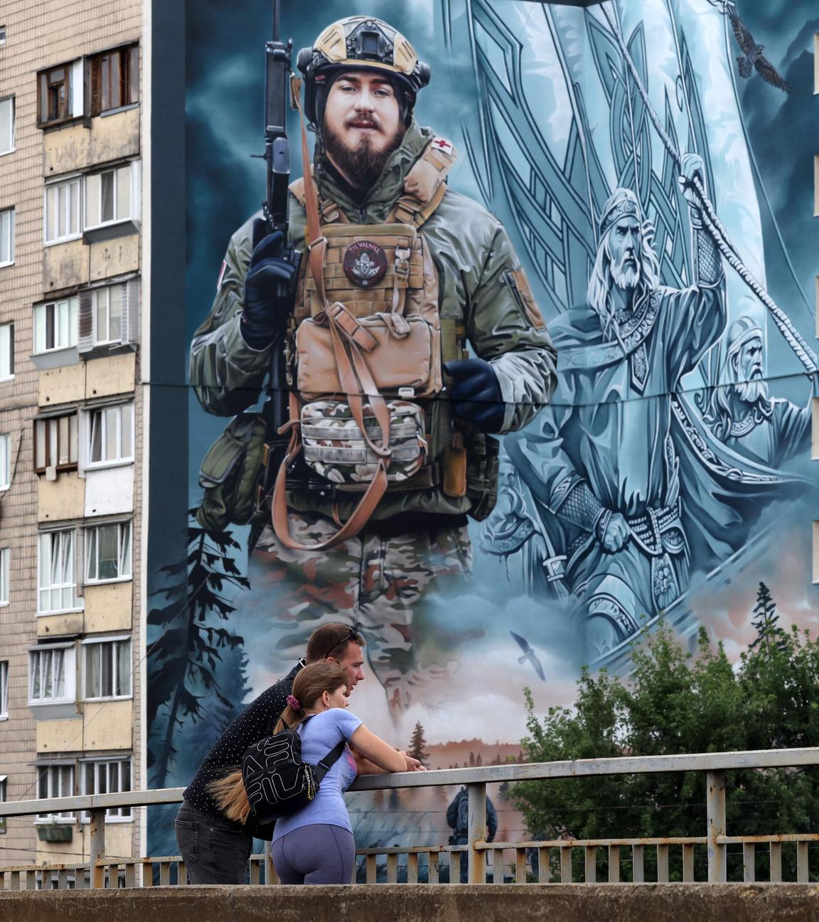 Fußgänger stehen vor einem großen Wandgemälde eines ukrainischen Soldaten.