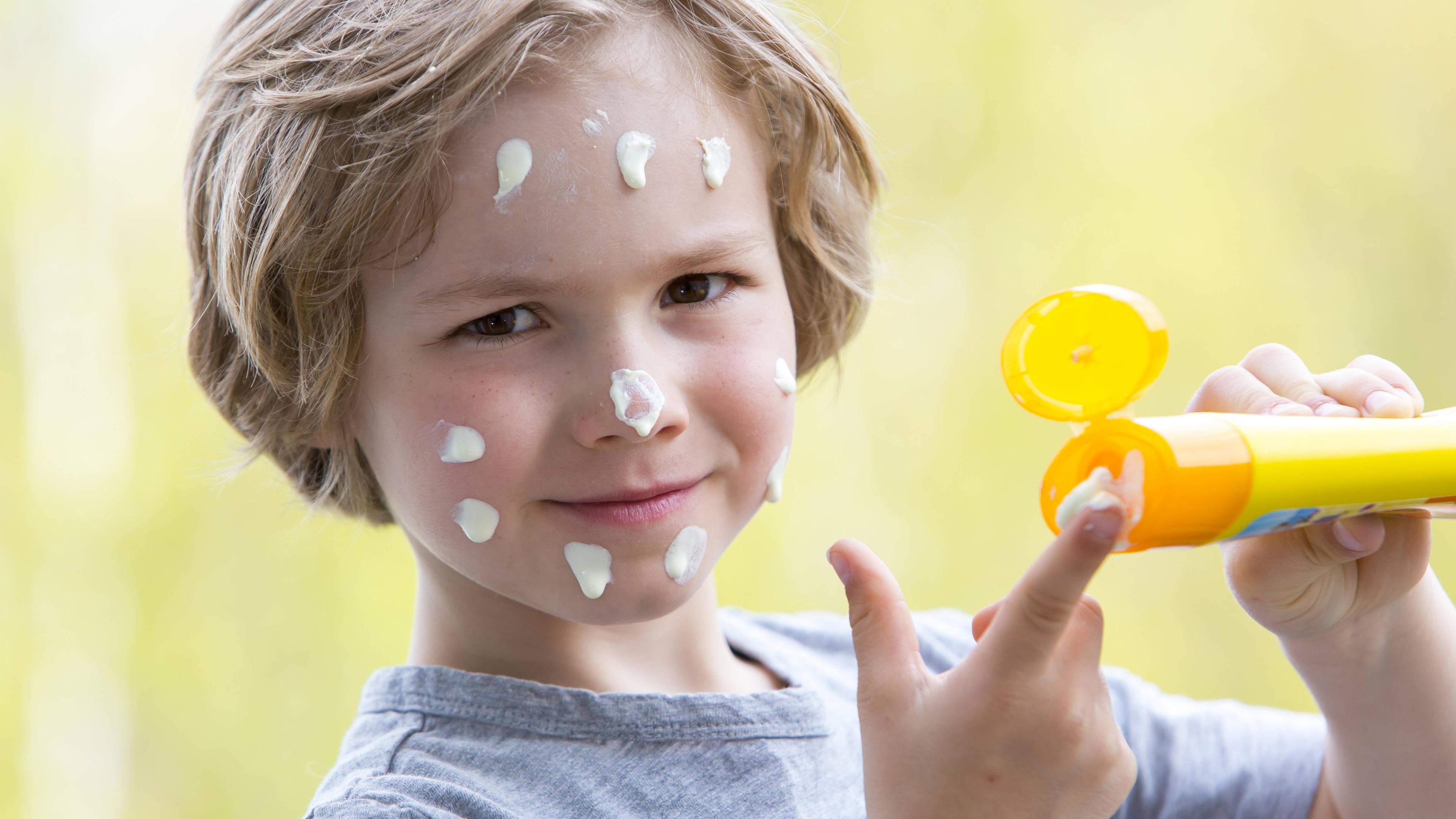 Junge mit Sonnencreme im Gesicht und Sonnencremeflasche in der Hand