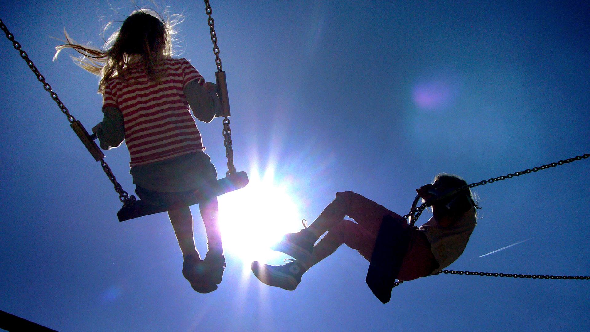 Zwei Kinder schaukeln auf dem Spielplatz