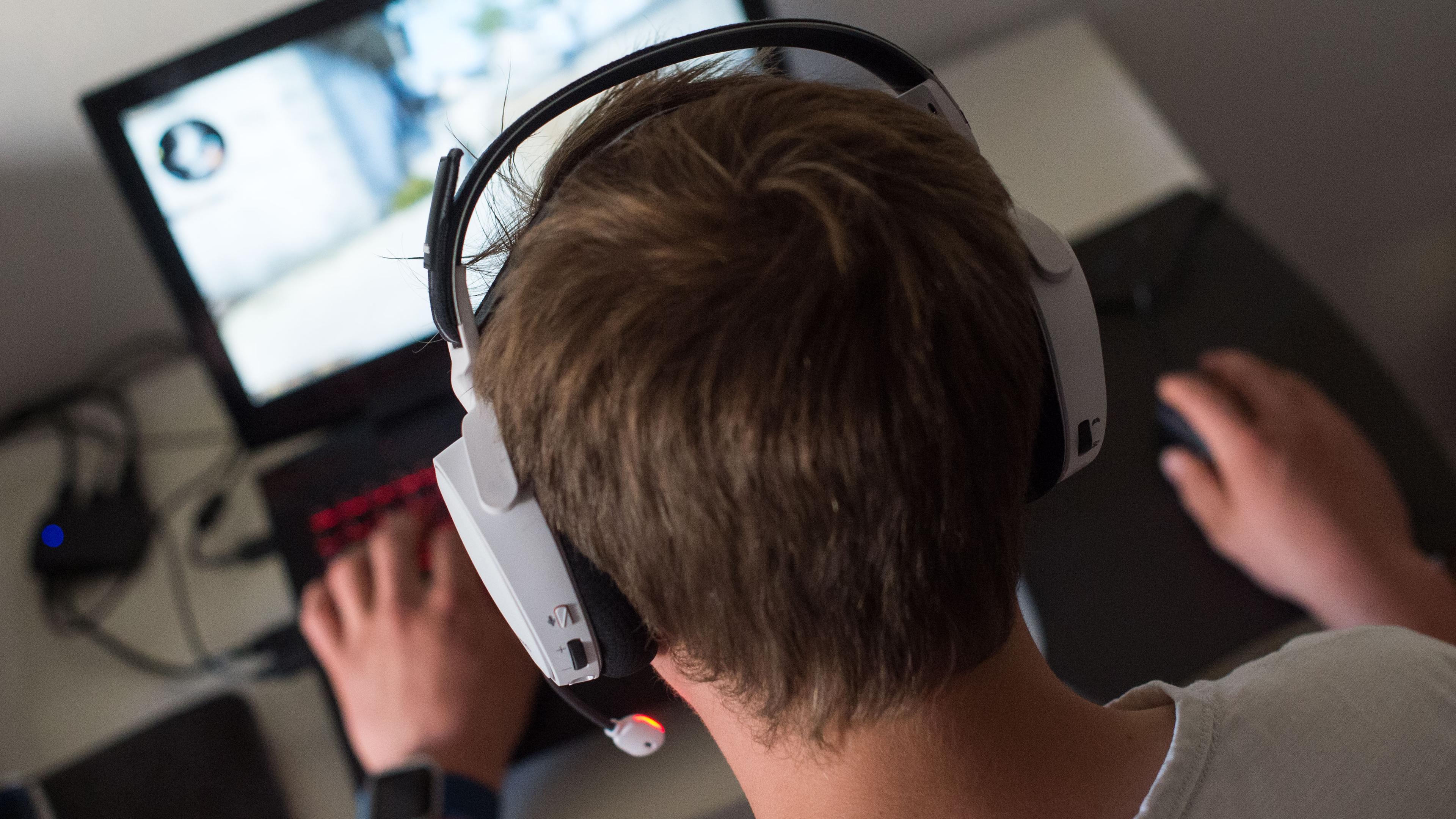 Ein Jugendlicher sitzt mit einem Headset vor einem Laptop und spielt ein Online-Computerspiel.