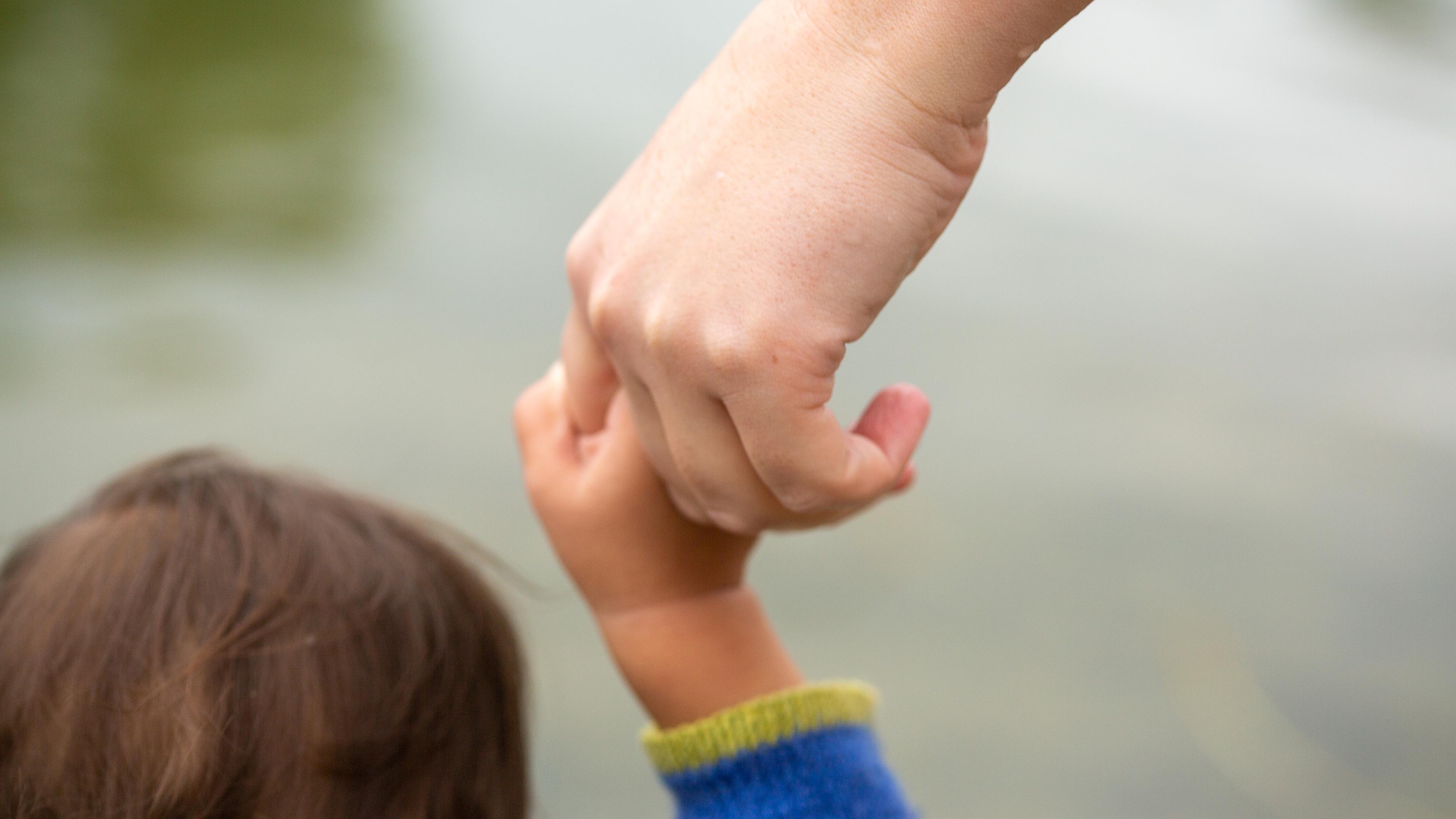 Ein Kind hält die Hand eines Elternteils.