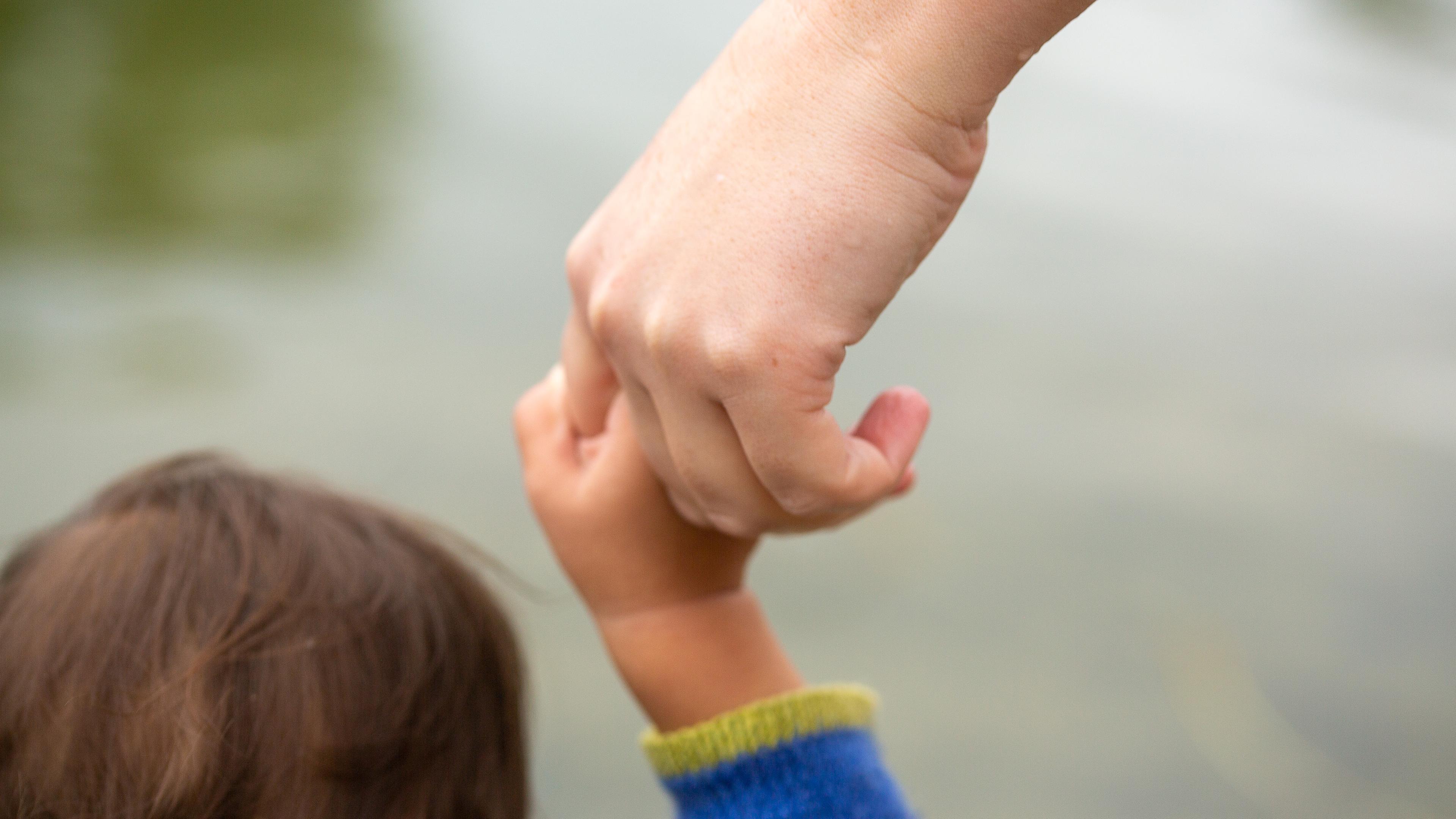 Eine erwachsene Person hält die Hand eines Kindes.