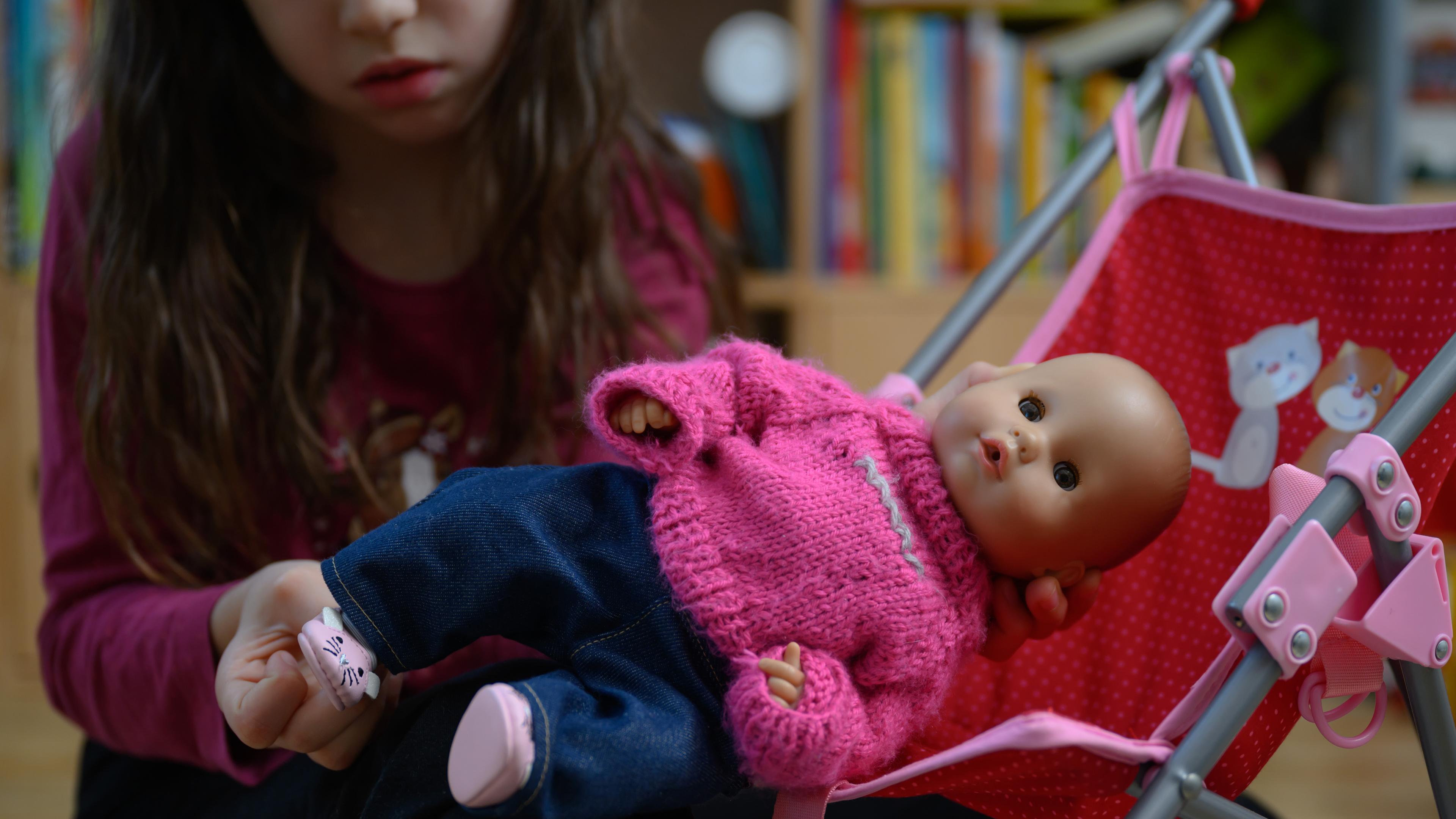 Symbolbild: Ein Mädchen spielt mit einer Puppe in rosa Kleidung.