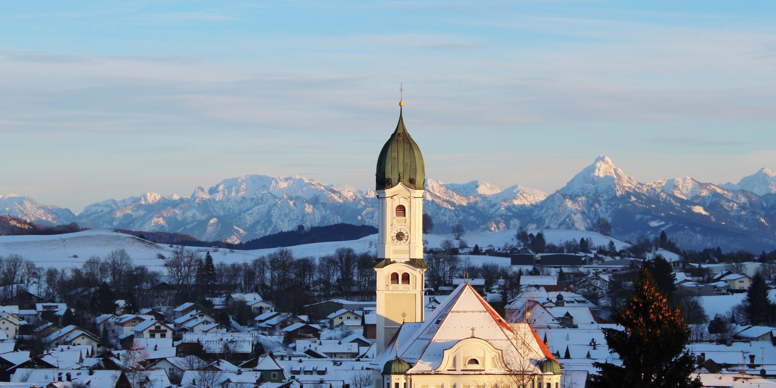 Ein Kirchturm vor einem Berg-Panorama.