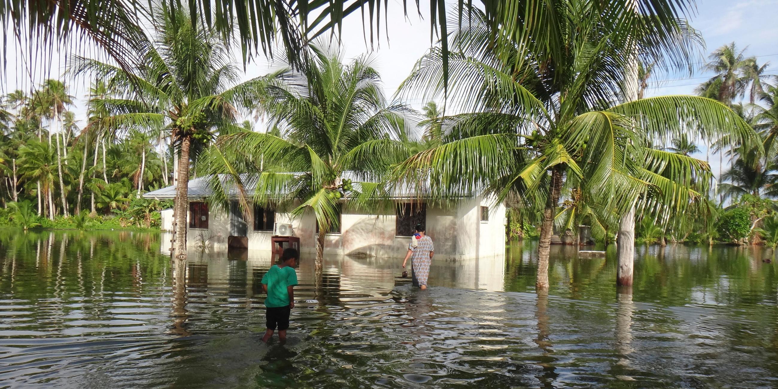 21, 2015 photo released by bikini atoll local government, a woman and a child walk through knee deep water to reach their home during a king tide event on kili in the marshall islands