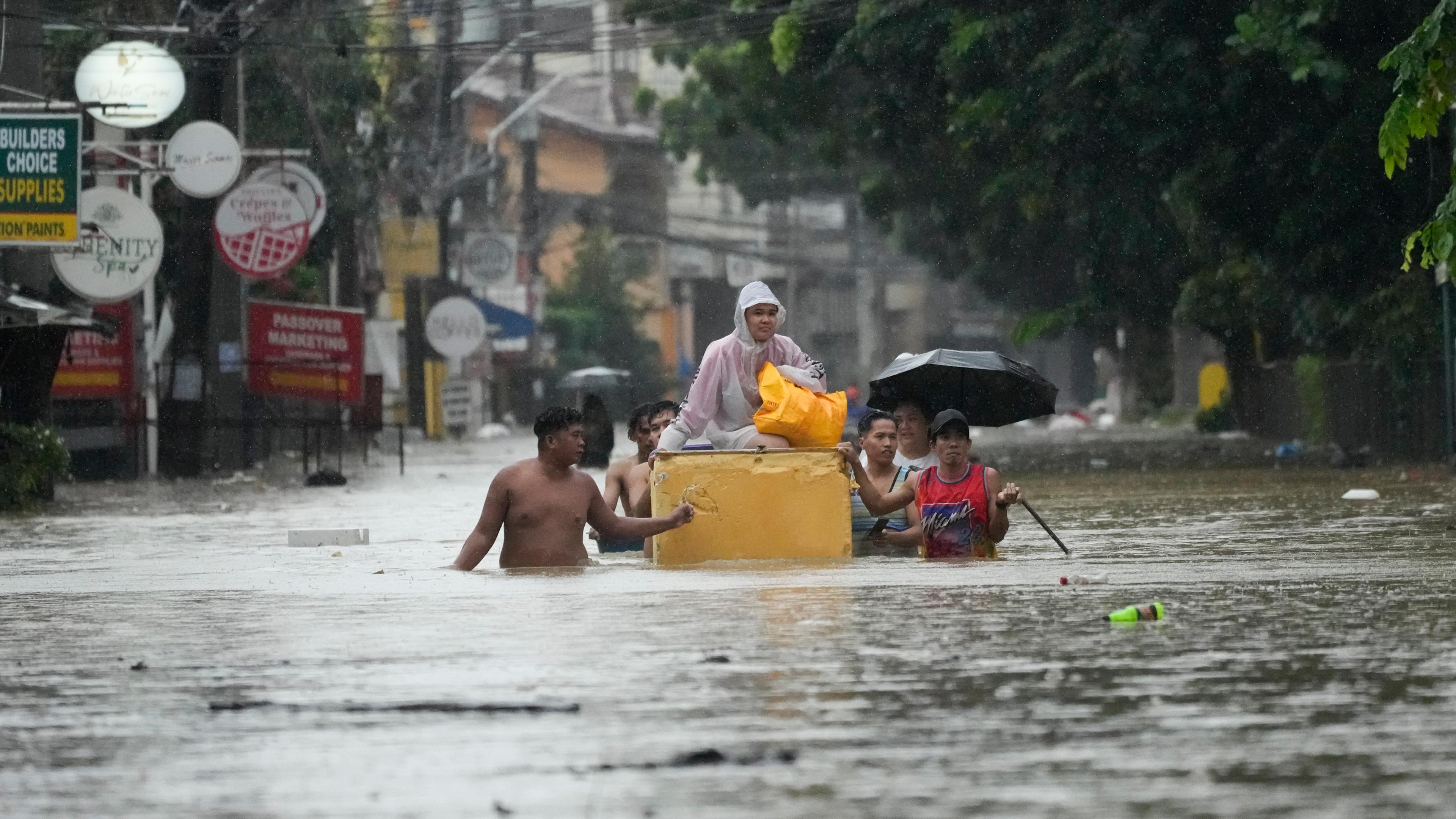 Ein paar Anwohner der philippinischen Stadtgemeinde Cainta durchqueren deren überflutete Straßen, das Wasser reicht ihnen zum Teil über die Hüfte.