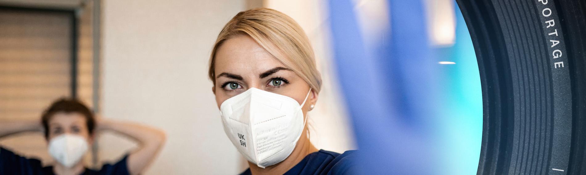 Krankenschwester hebt eine Hand zum Stopp, eine andere ist unscharf im Hintergrund zu sehen.