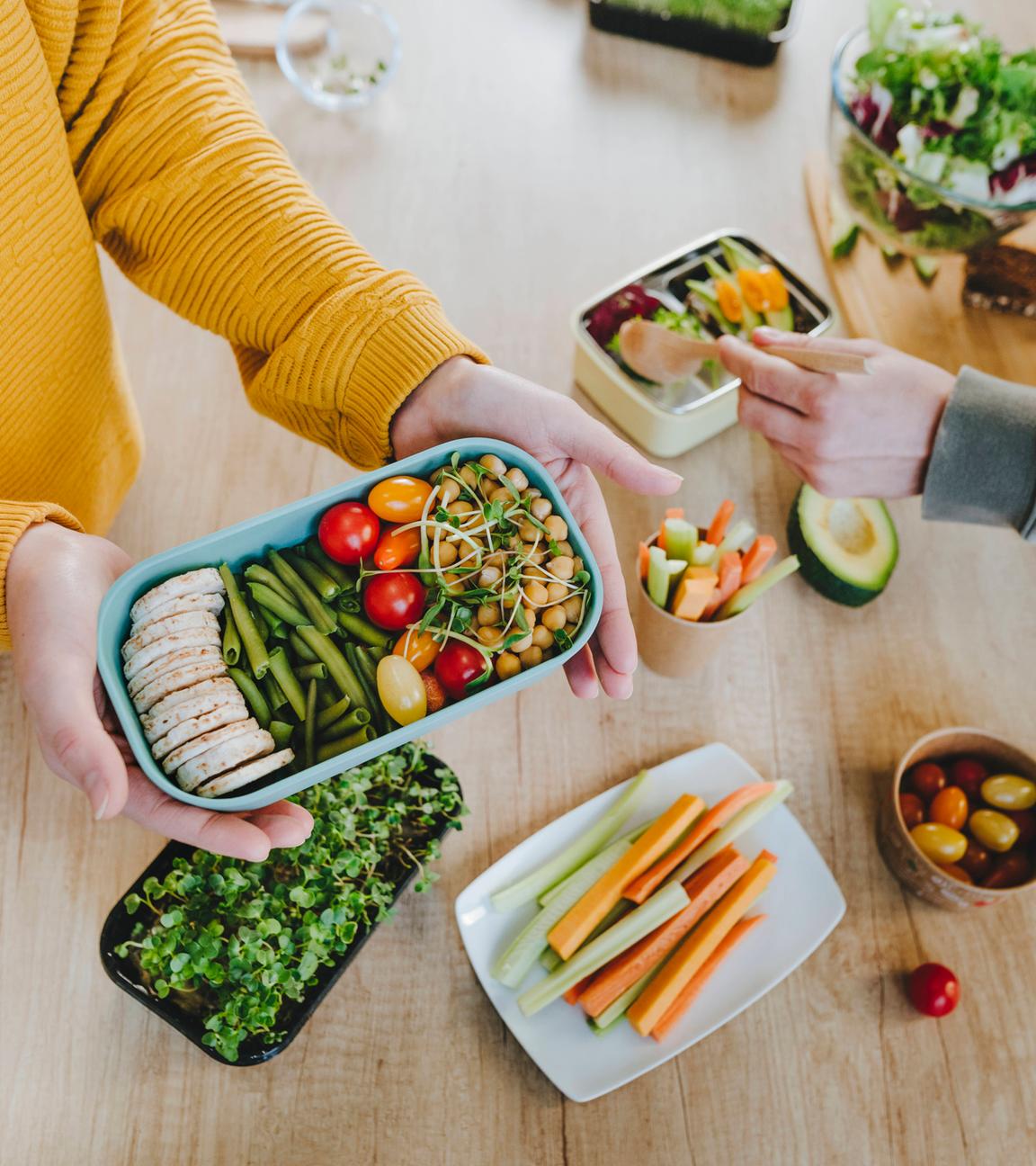 Zwei Menschen bereiten Essen in der Küche zu und füllen es in Vorratsbehälter.